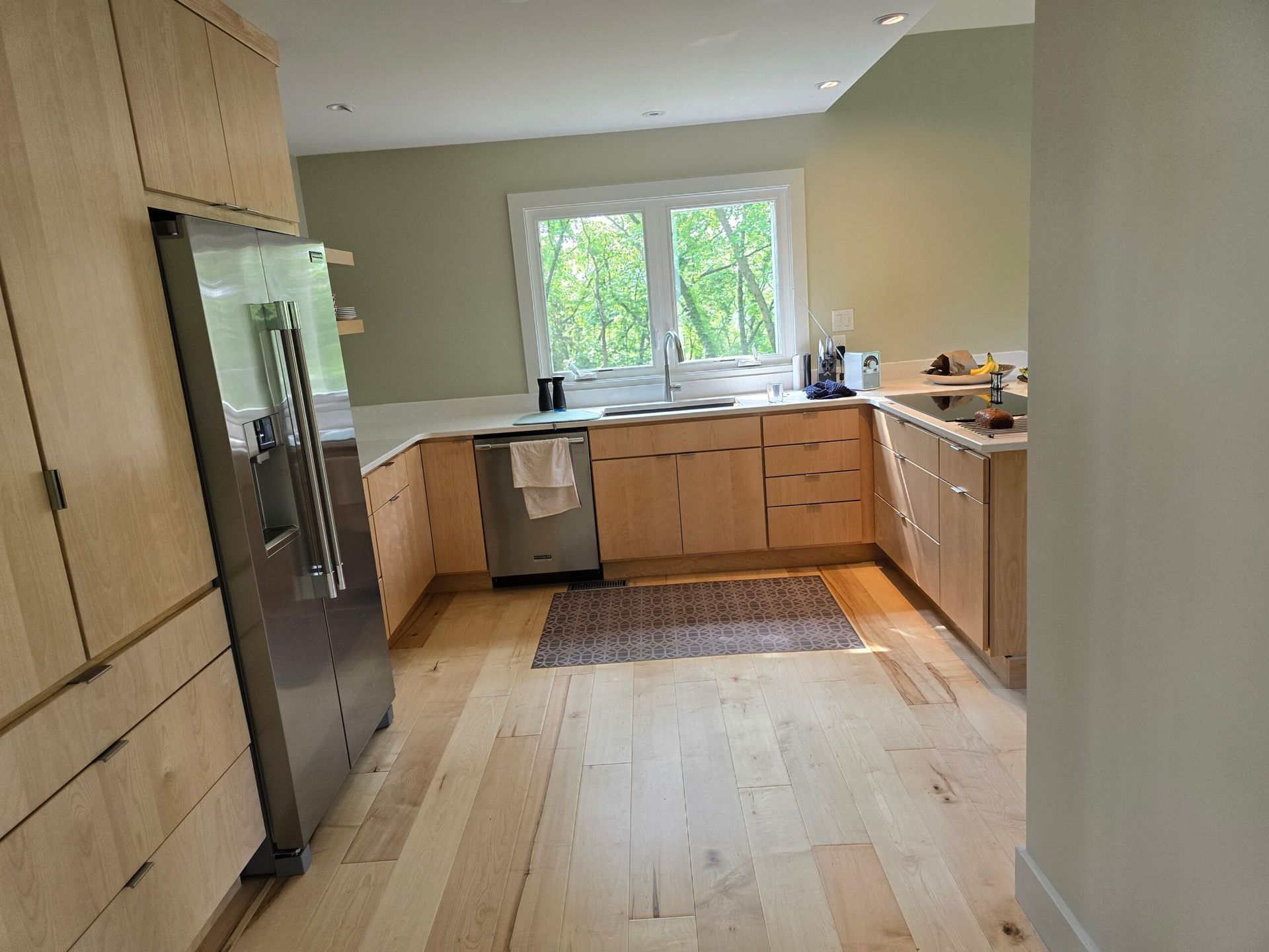 Modern kitchen with light wood cabinets, stainless fridge, island, and a window above the sink