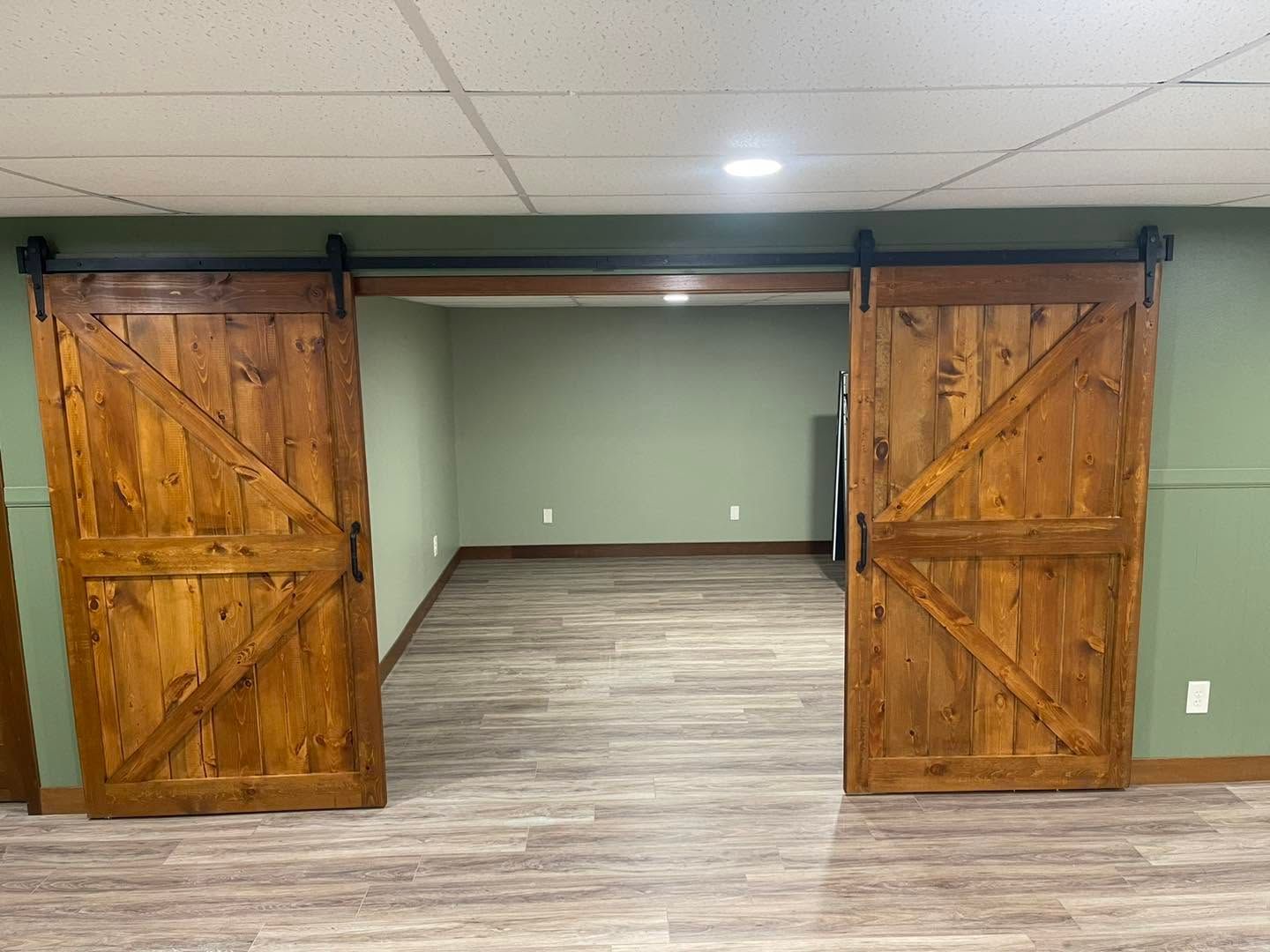 Open barn-style wooden double doors leading into a green room with gray flooring.