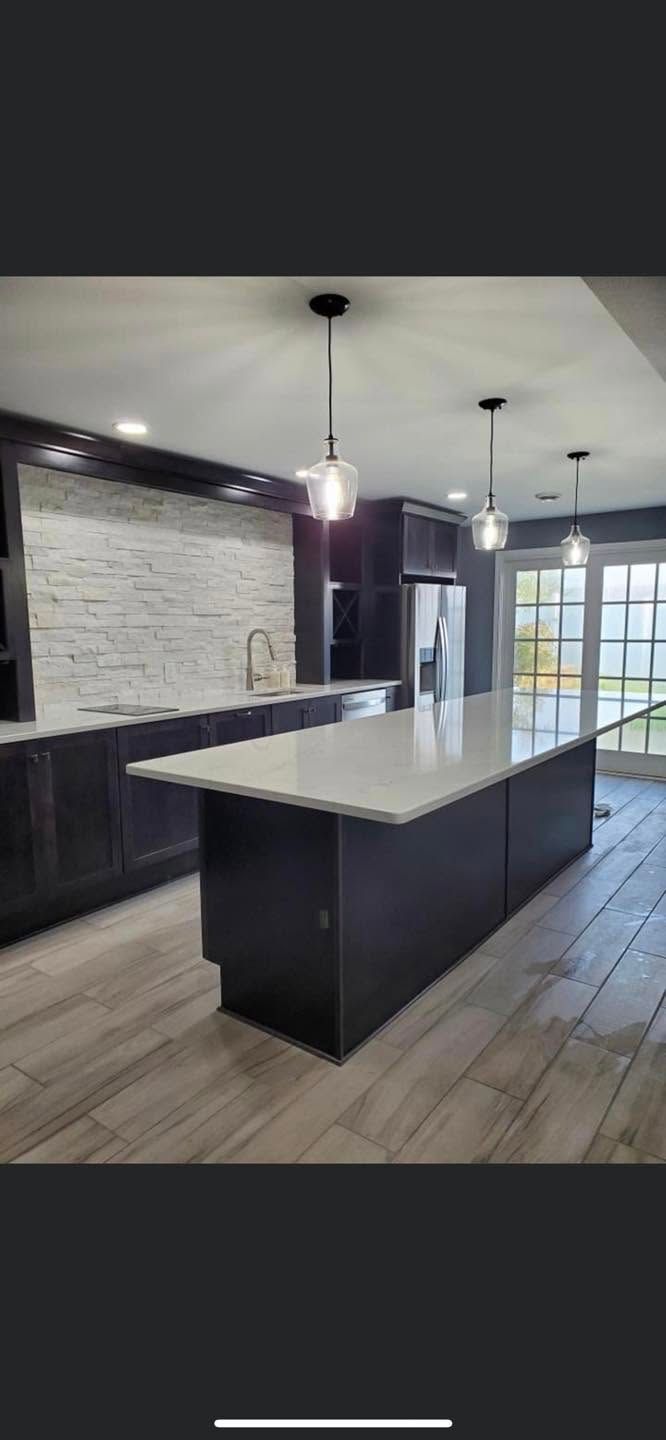 Modern kitchen with a large island, dark cabinets, white countertops, and wood plank flooring.