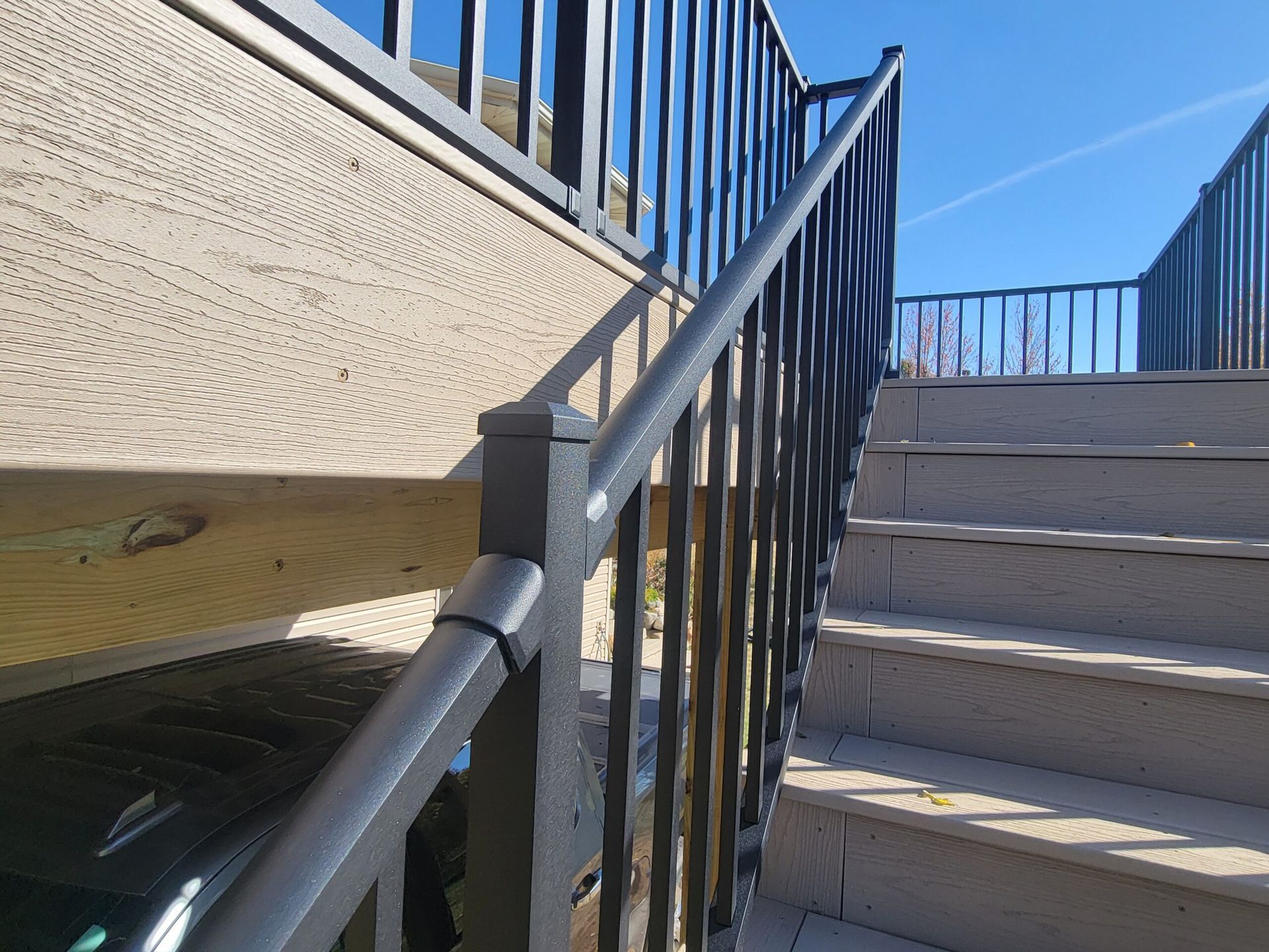 Outdoor concrete stairs with black metal railings beside a stucco wall under a blue sky