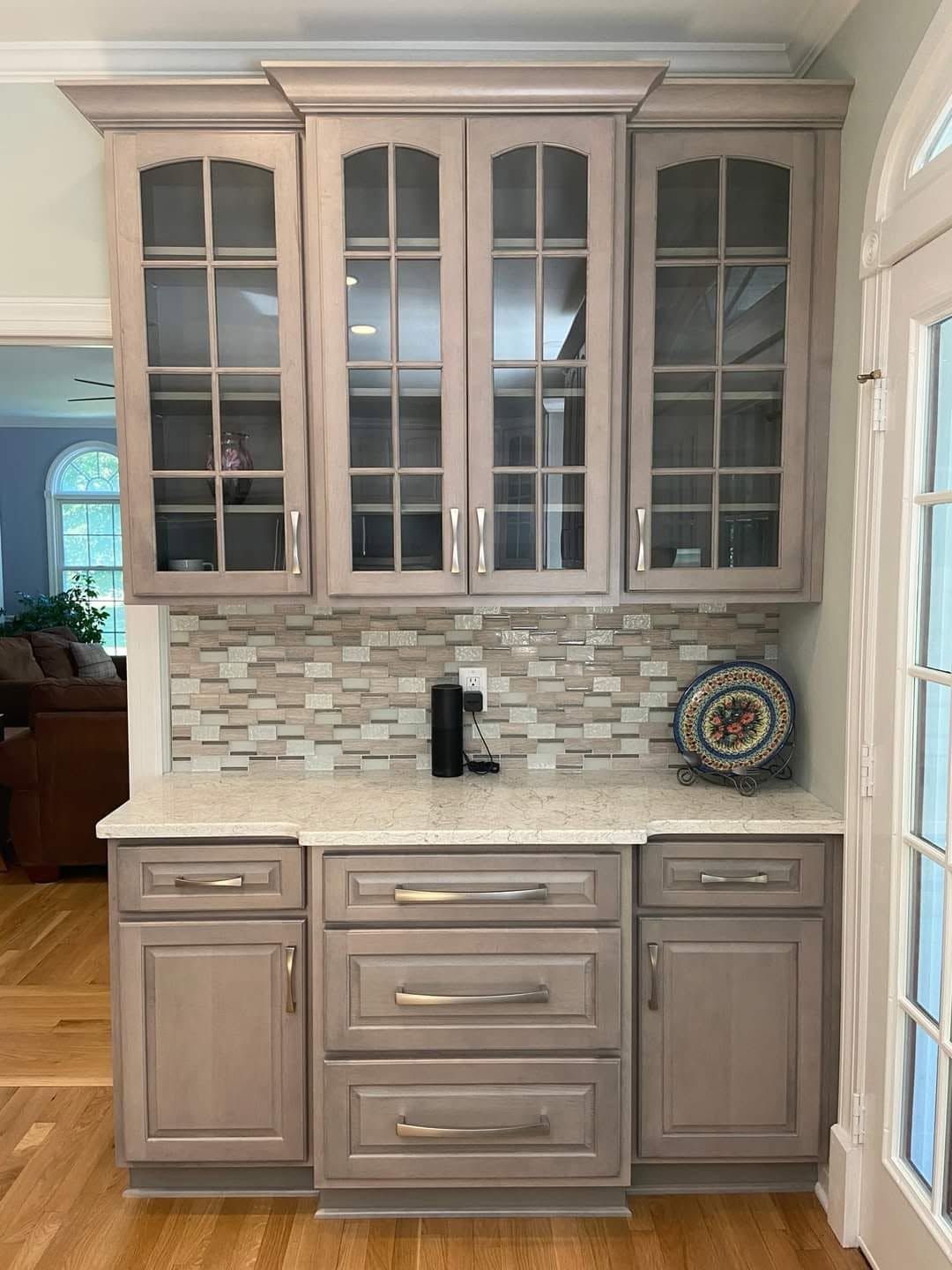 Built-in kitchen hutch with glass-front cabinets, mosaic tile backsplash, and beige wood finish.