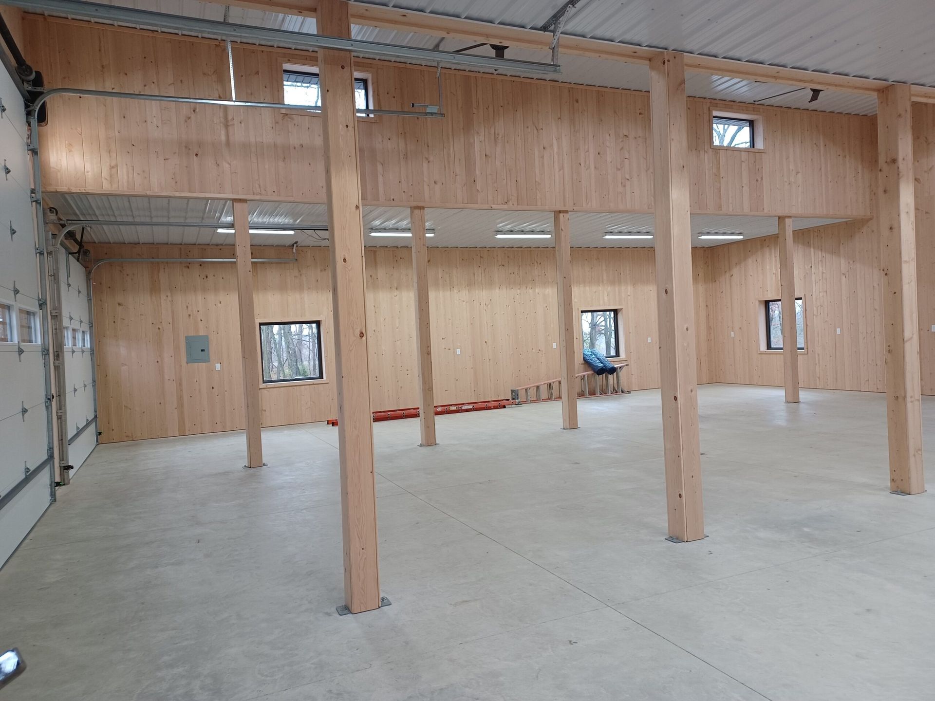 Empty wooden warehouse interior with exposed beams, concrete floor, and large garage door.