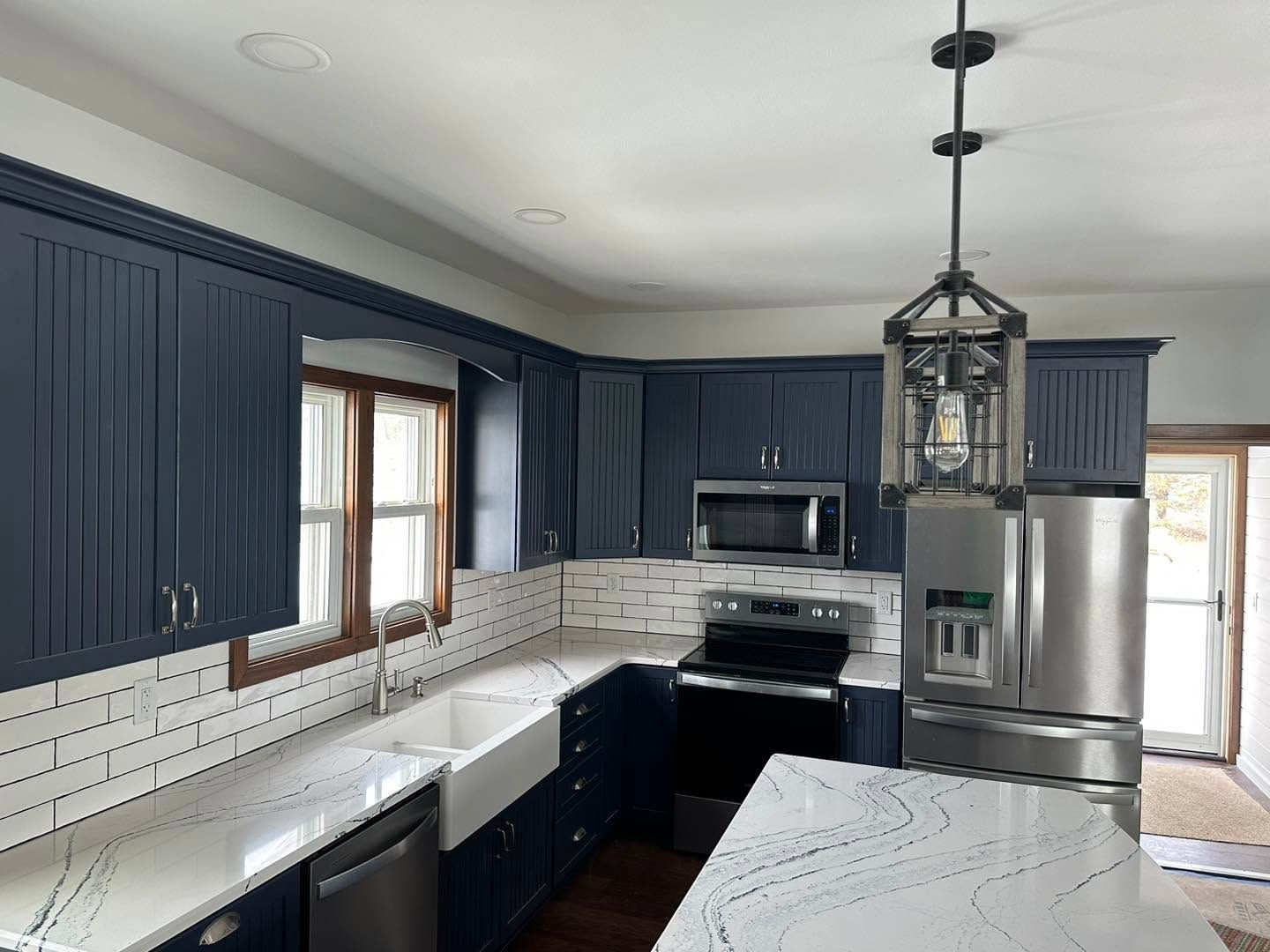 Modern kitchen with navy cabinets, white countertops, stainless steel appliances, and a large island