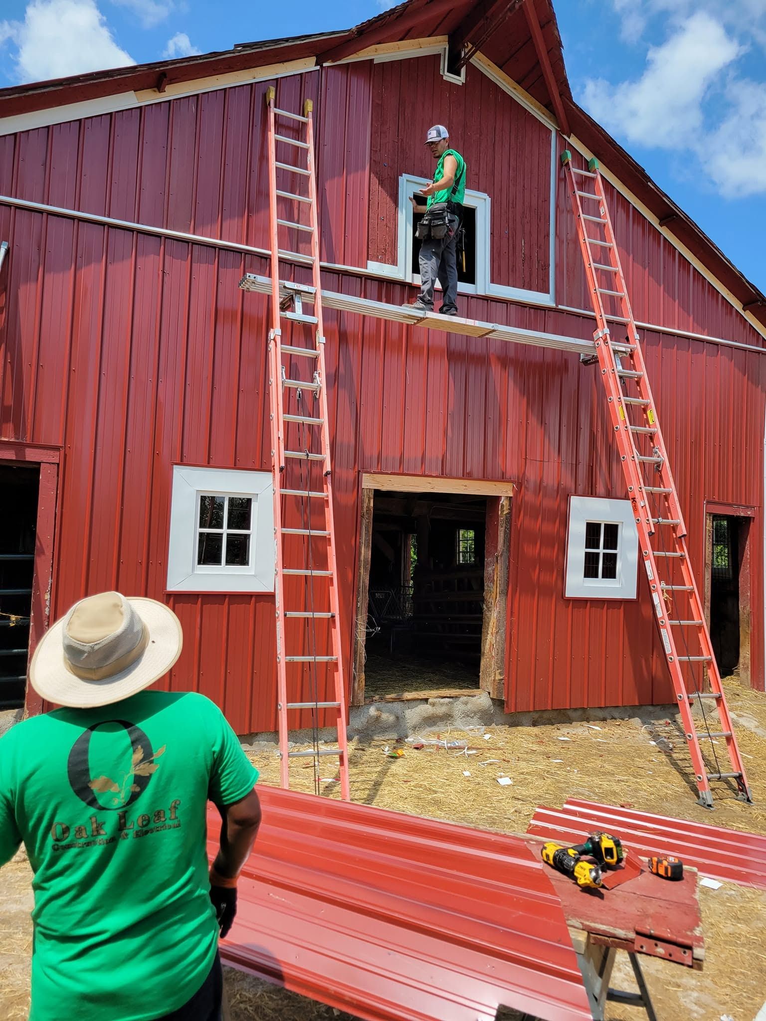 Workers on ladders painting a red barn; one stands on a lift near the upper window.