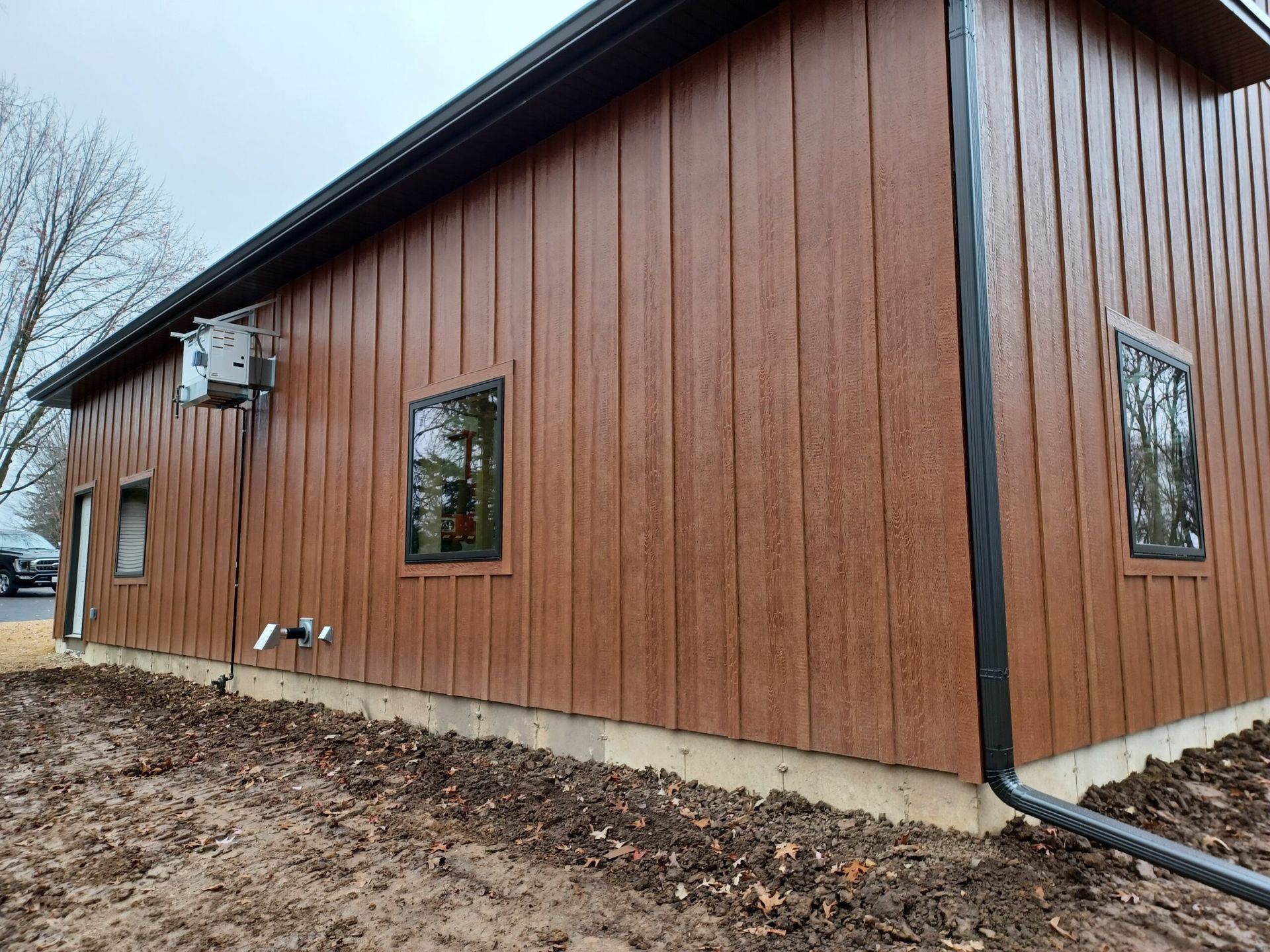 Brown metal-sided building exterior with small windows and concrete foundation on a cloudy day