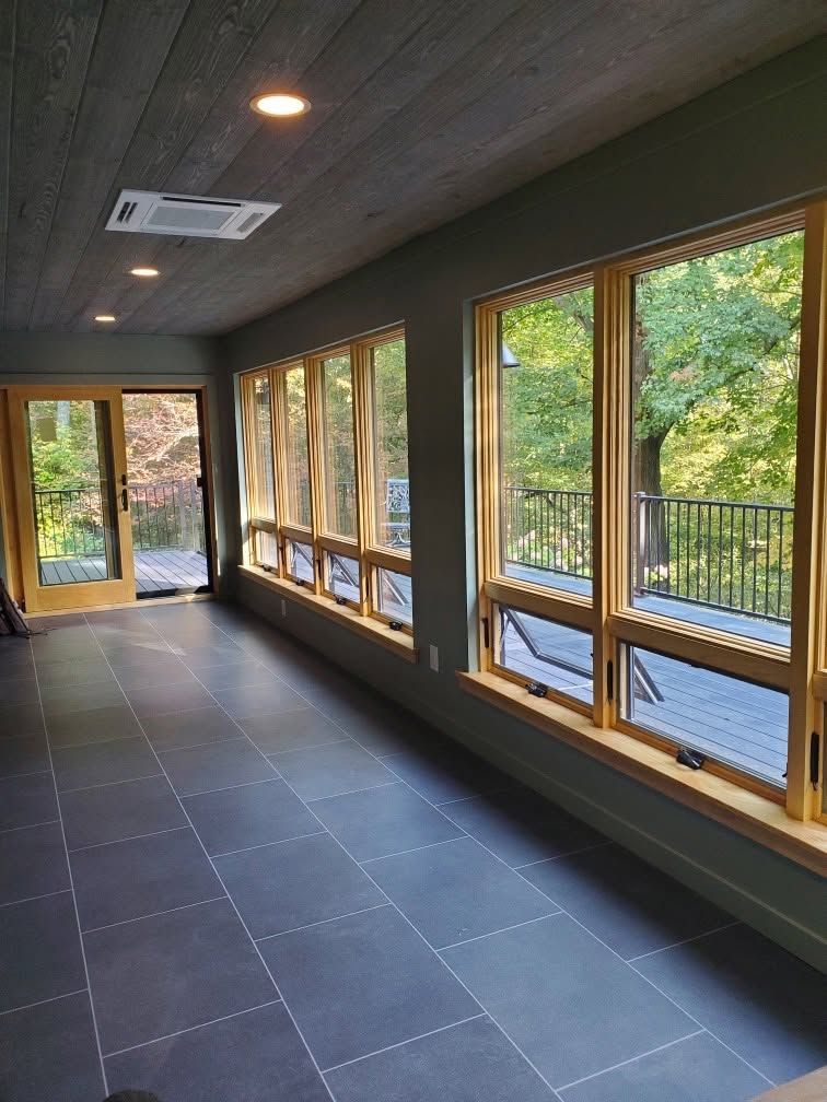 Empty sunroom with tiled floor and large windows overlooking trees and a deck