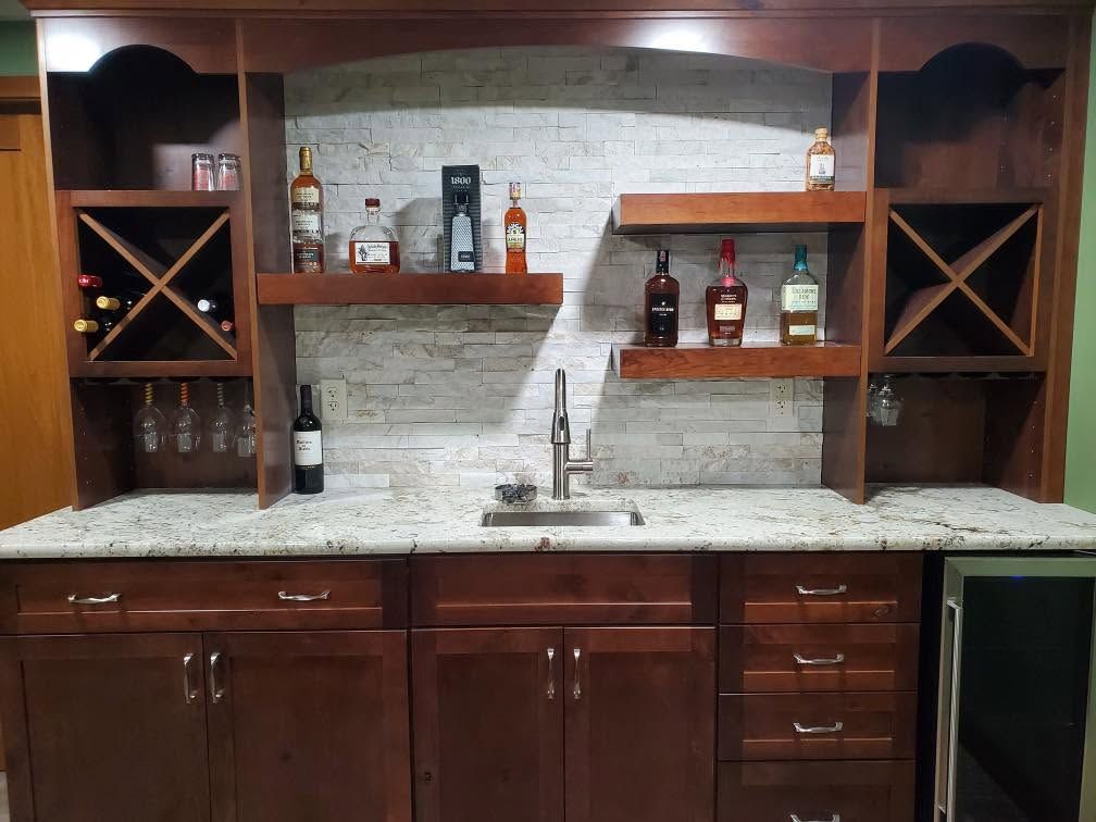 Wooden kitchen wet bar with shelves, wine rack, sink, and dark wood cabinets beneath a stone backsplash