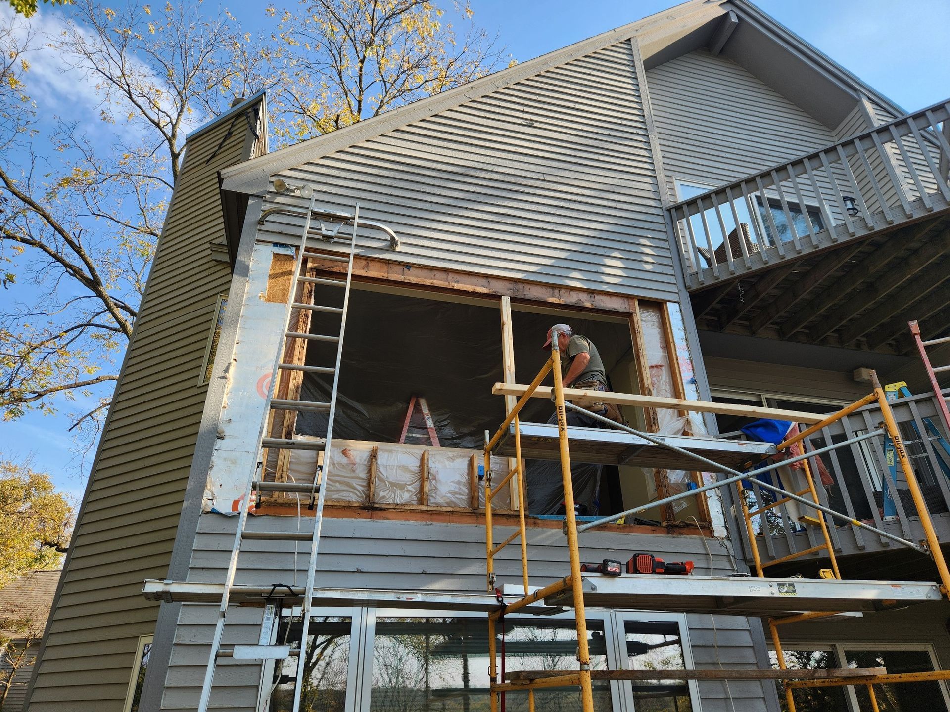 House under renovation with workers on scaffolding and exposed siding under a blue sky