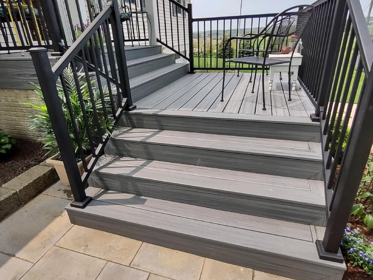 Black metal outdoor stairs with gray steps and railing leading to a small patio with chairs and a garden view