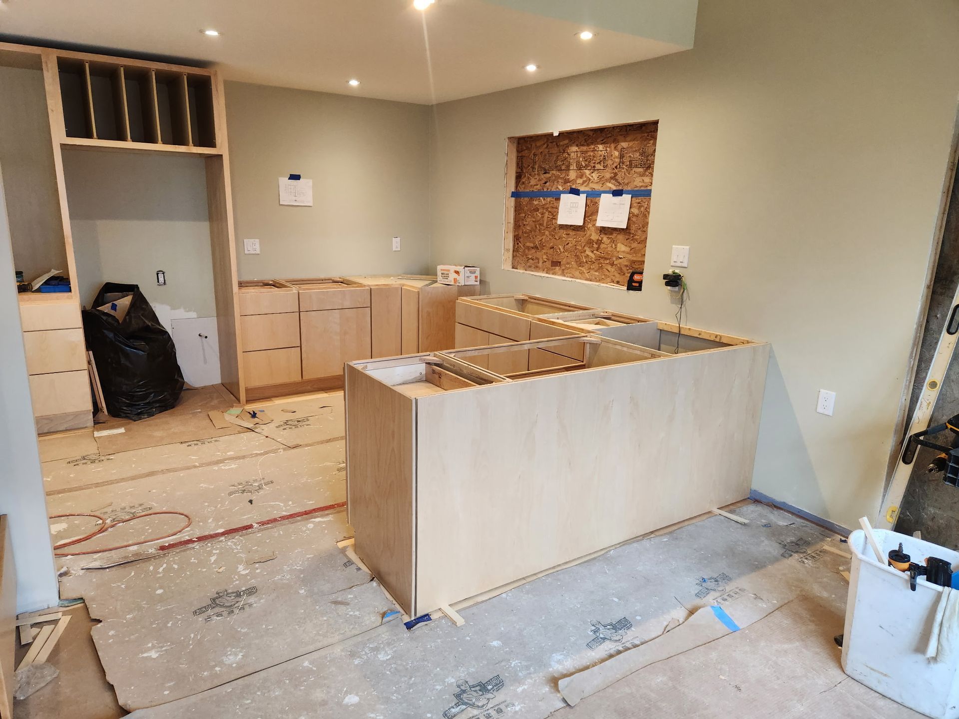 Unfinished kitchen remodel with light wood cabinets, island, and exposed flooring under construction
