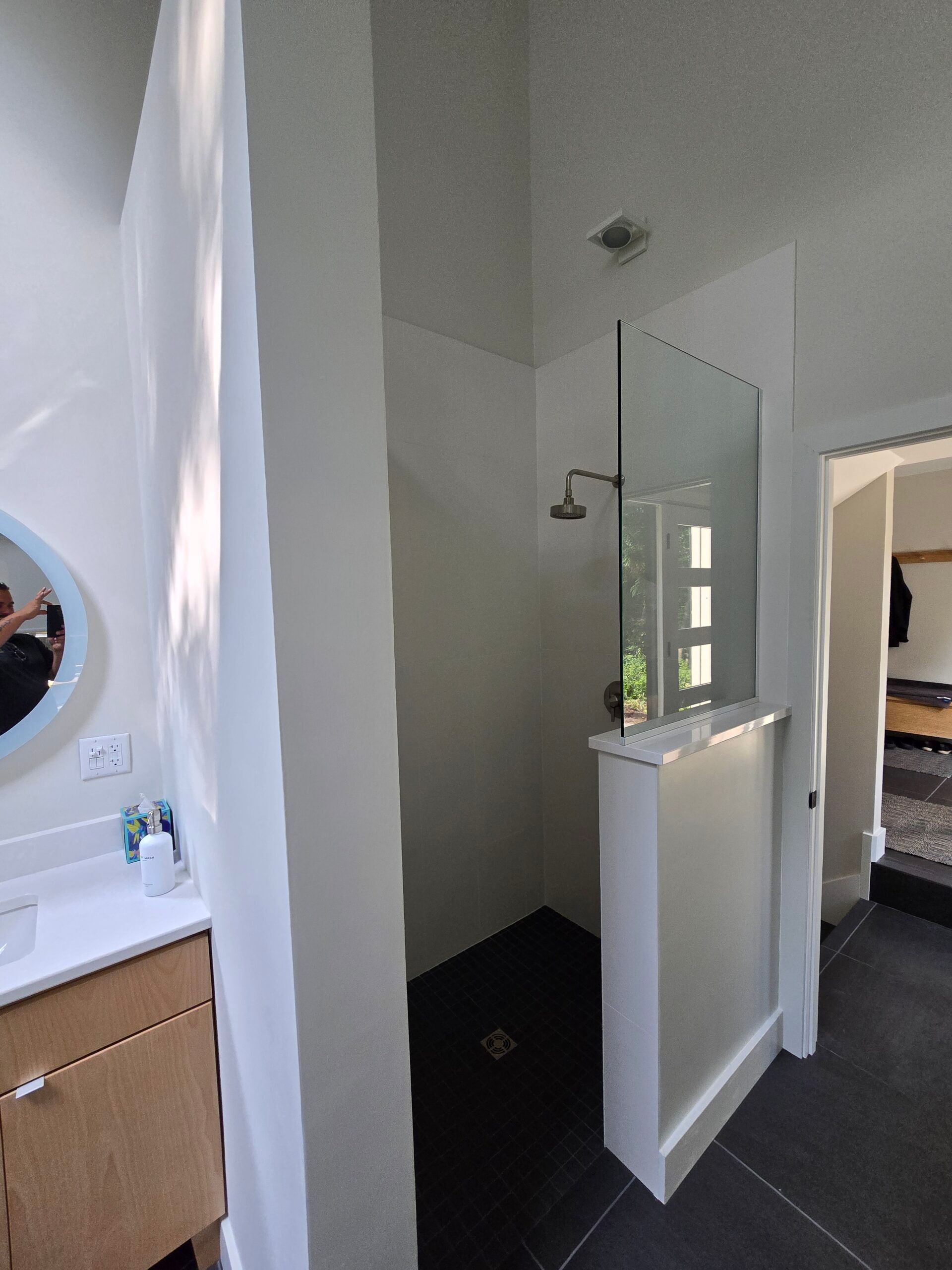 Bathroom with white walls, a vanity, wall mirror, and a doorway to a bedroom with a bed visible.