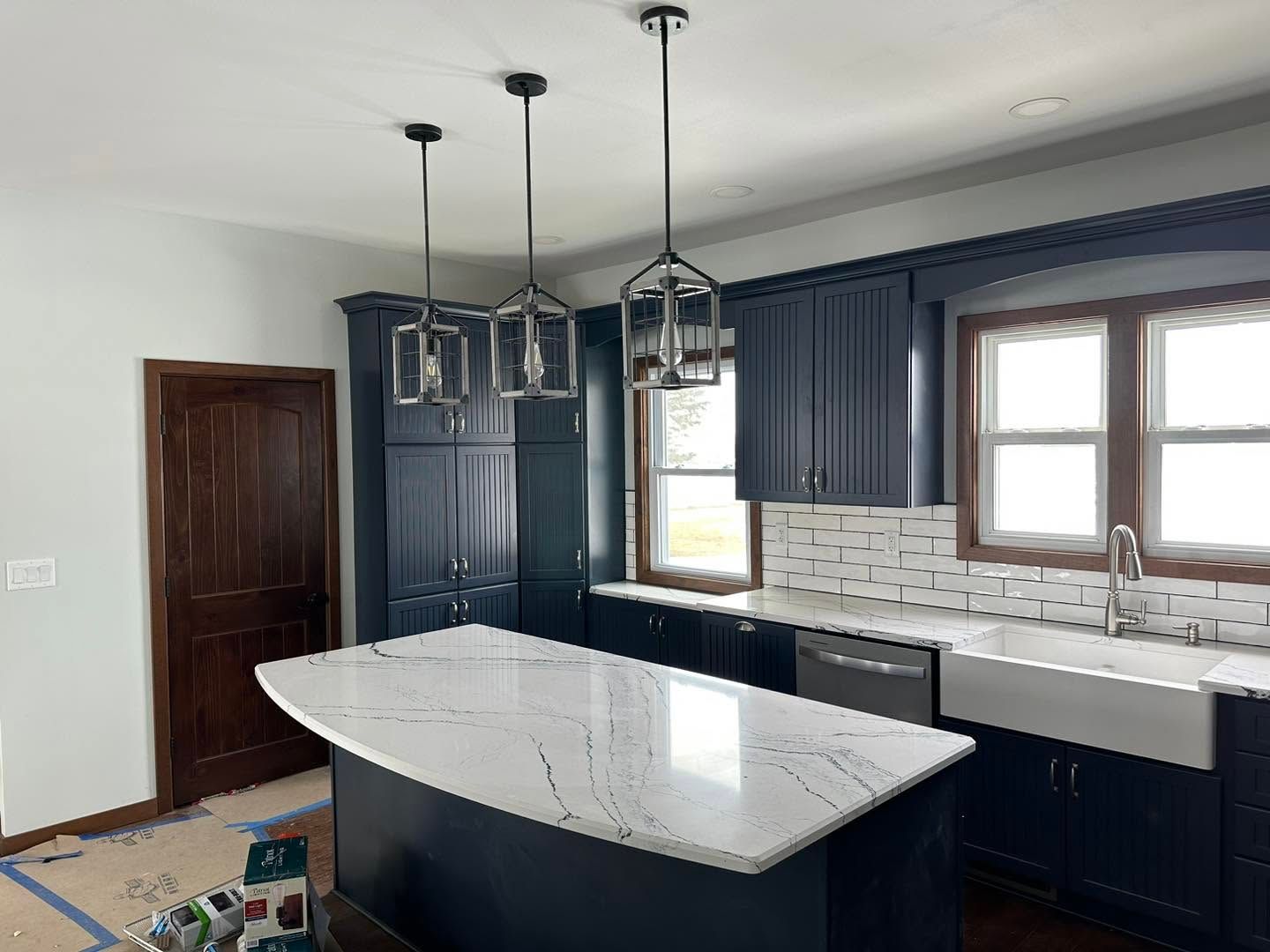 Modern kitchen with white island, dark cabinets, pendant lights, gray tile backsplash, and window above sink