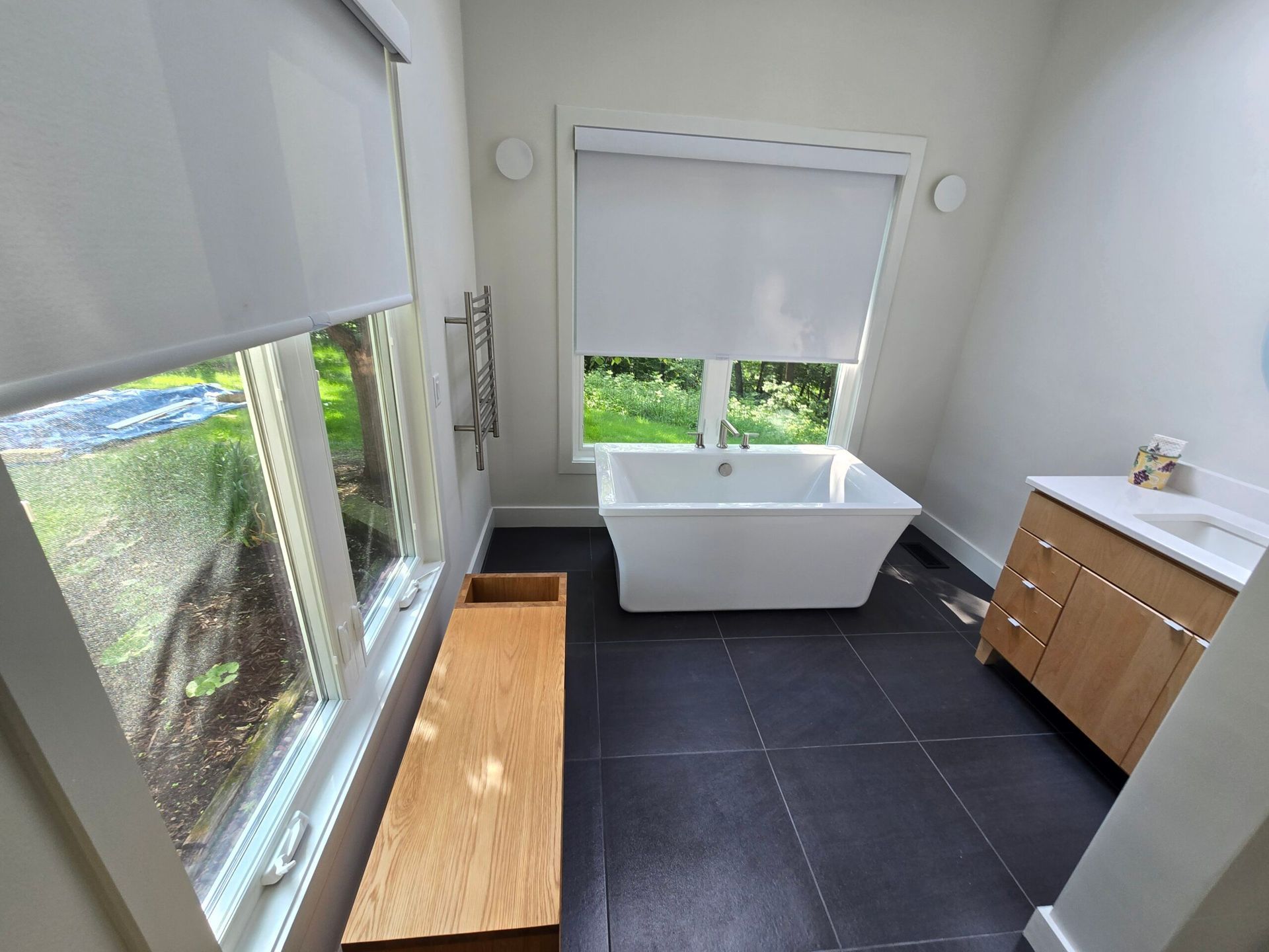 Modern bathroom with freestanding tub, black tile floor, large windows, and wood vanity cabinets
