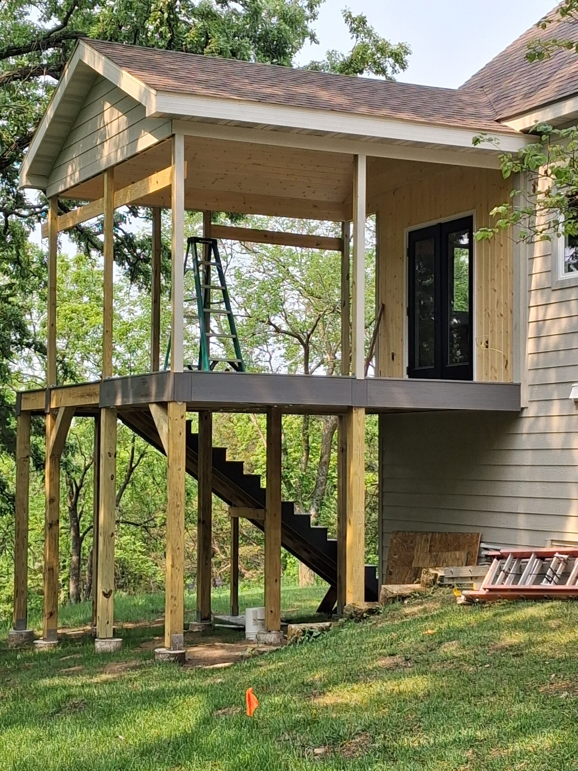Raised house porch with stairs, wooden posts, and a dark door on a grassy hillside.