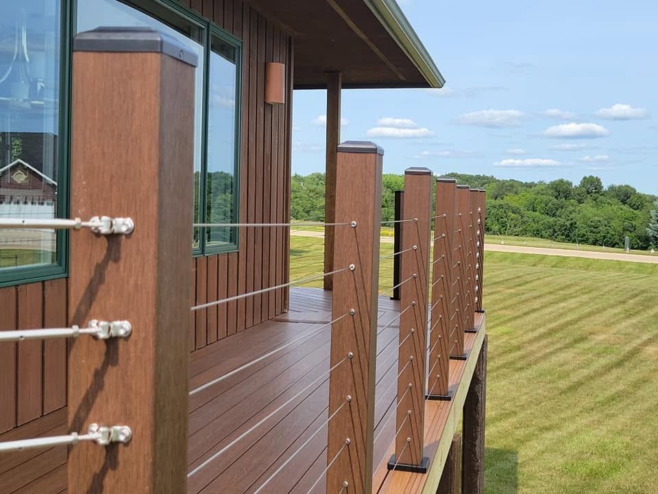 Wooden deck with glass railing beside a modern house, overlooking a mowed grassy field
