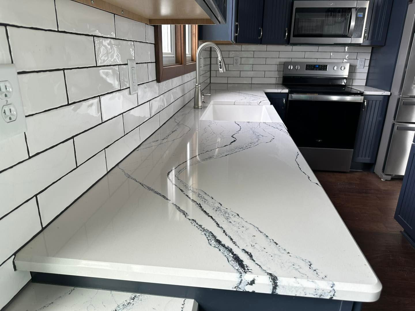 Modern kitchen with white marble-look countertop, white tile backsplash, black stove, and wood floor