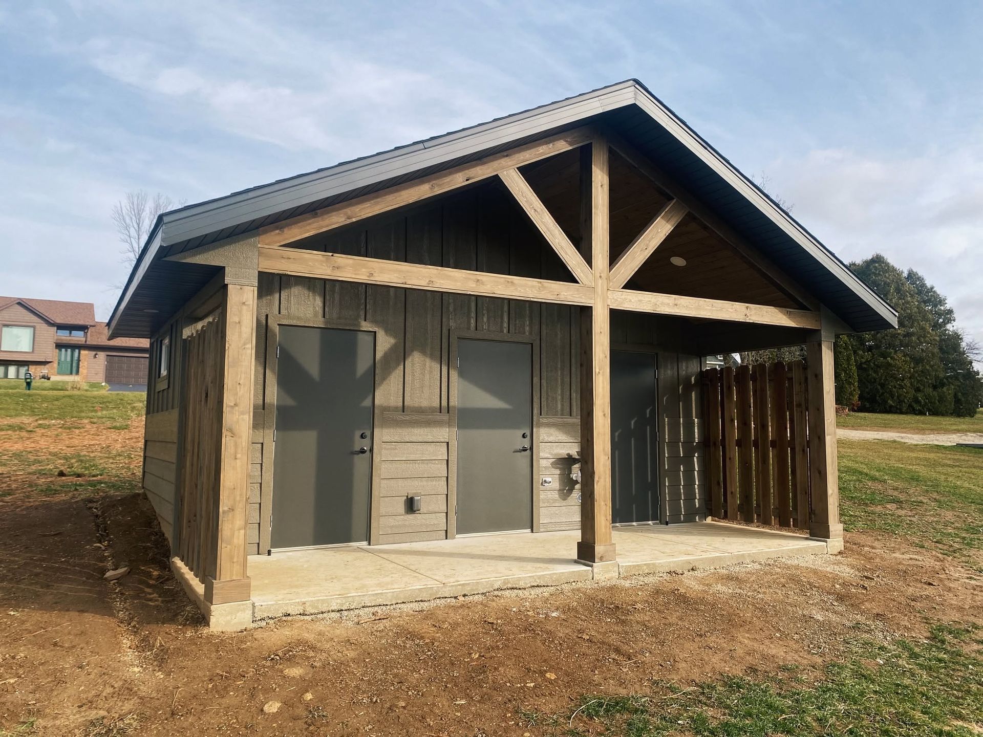 Small unfinished wooden shed with a gabled roof and open front on a dirt lot under a cloudy sky