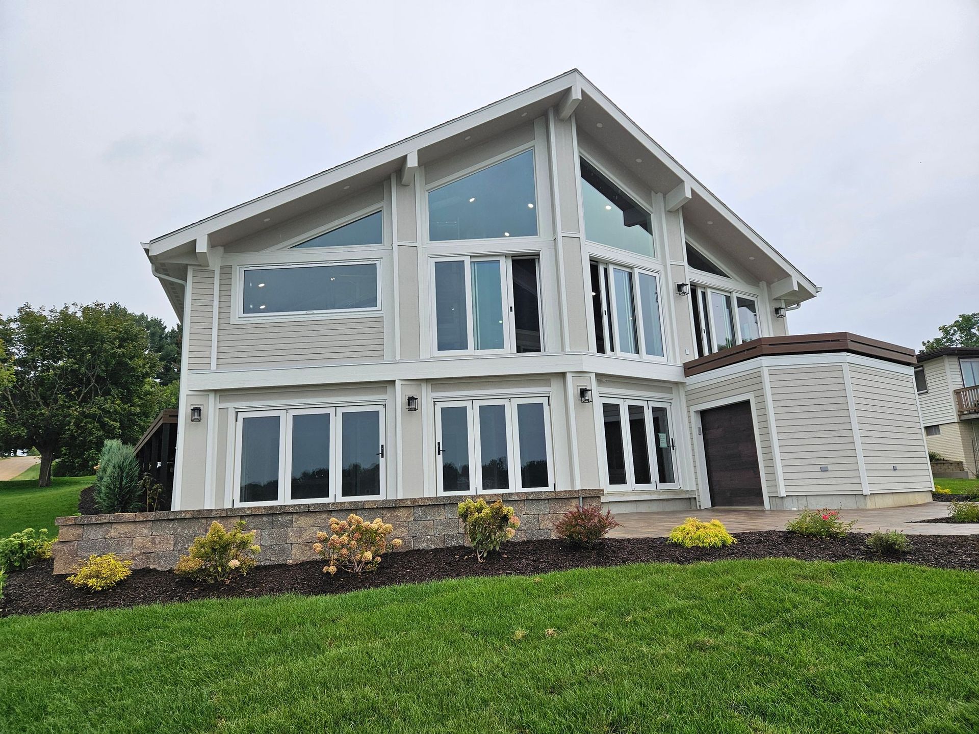 Modern two-story white house with large windows, stone accents, and a green lawn