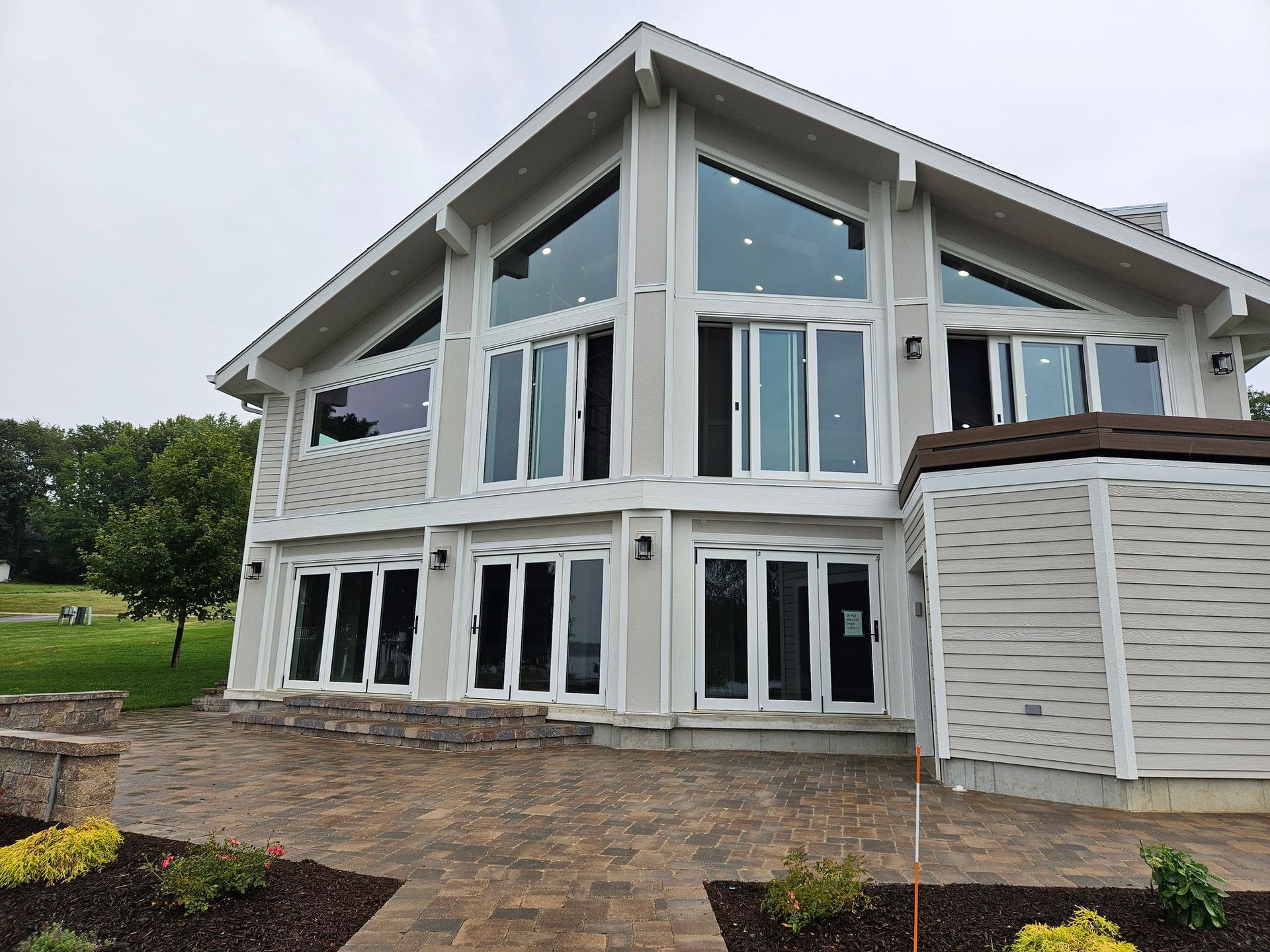 Modern white two-story house with large windows, sloped roof, and stone patio in a landscaped yard