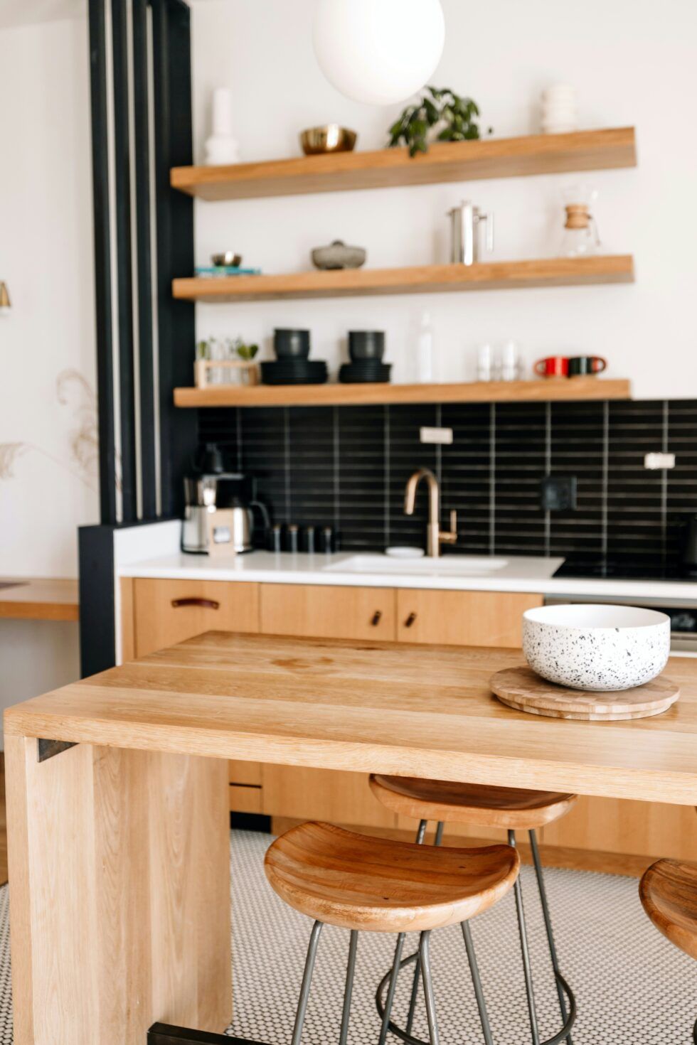 Modern kitchen with wood island, black tile backsplash, open shelves, and two stools