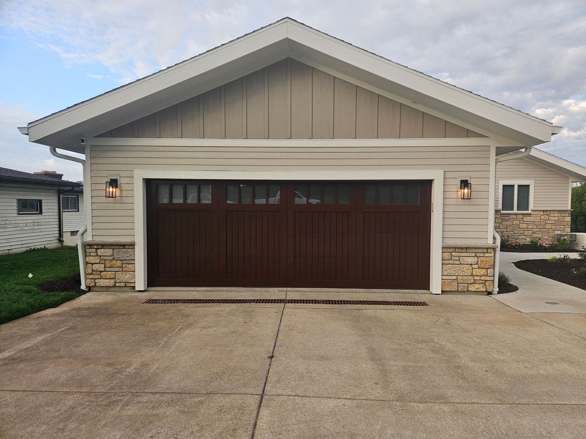 Single-story beige house with dark brown garage door and concrete driveway under a cloudy sky