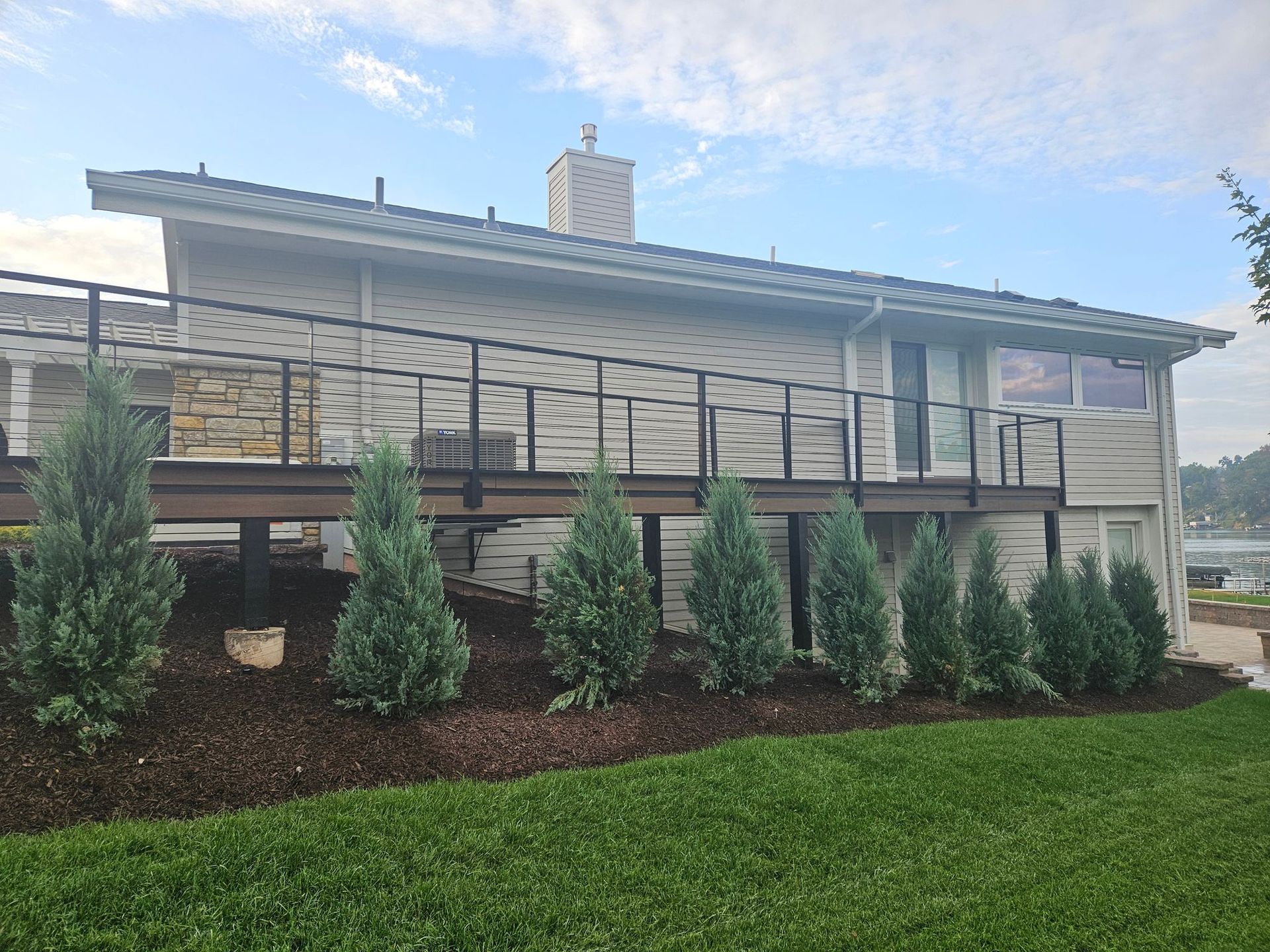 Modern house with stone exterior, black railing, and landscaped front yard with shrubs and green lawn