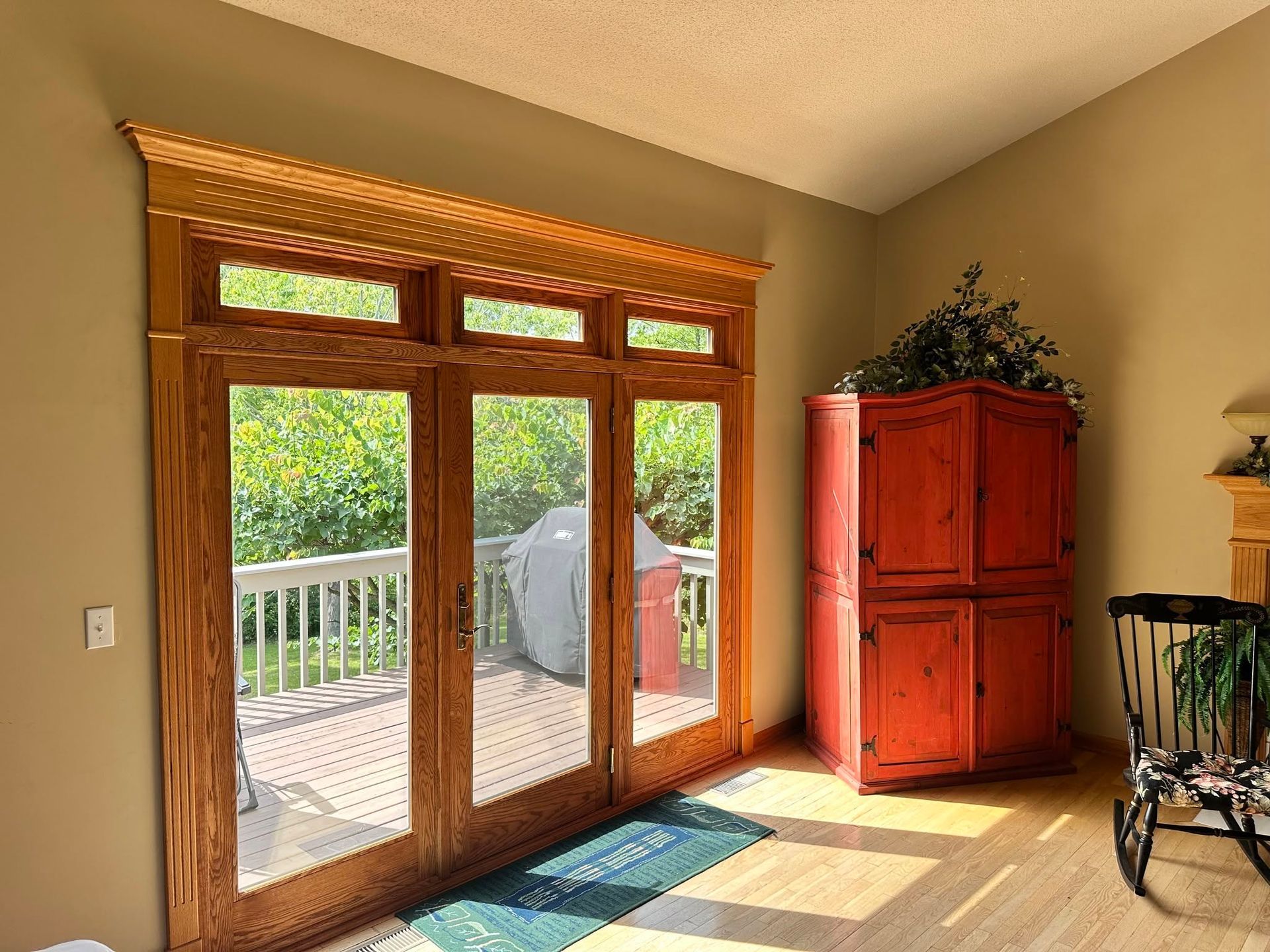 Sunlit room with wood-framed glass doors opening to a deck, red cabinet, and bicycle wheel at right