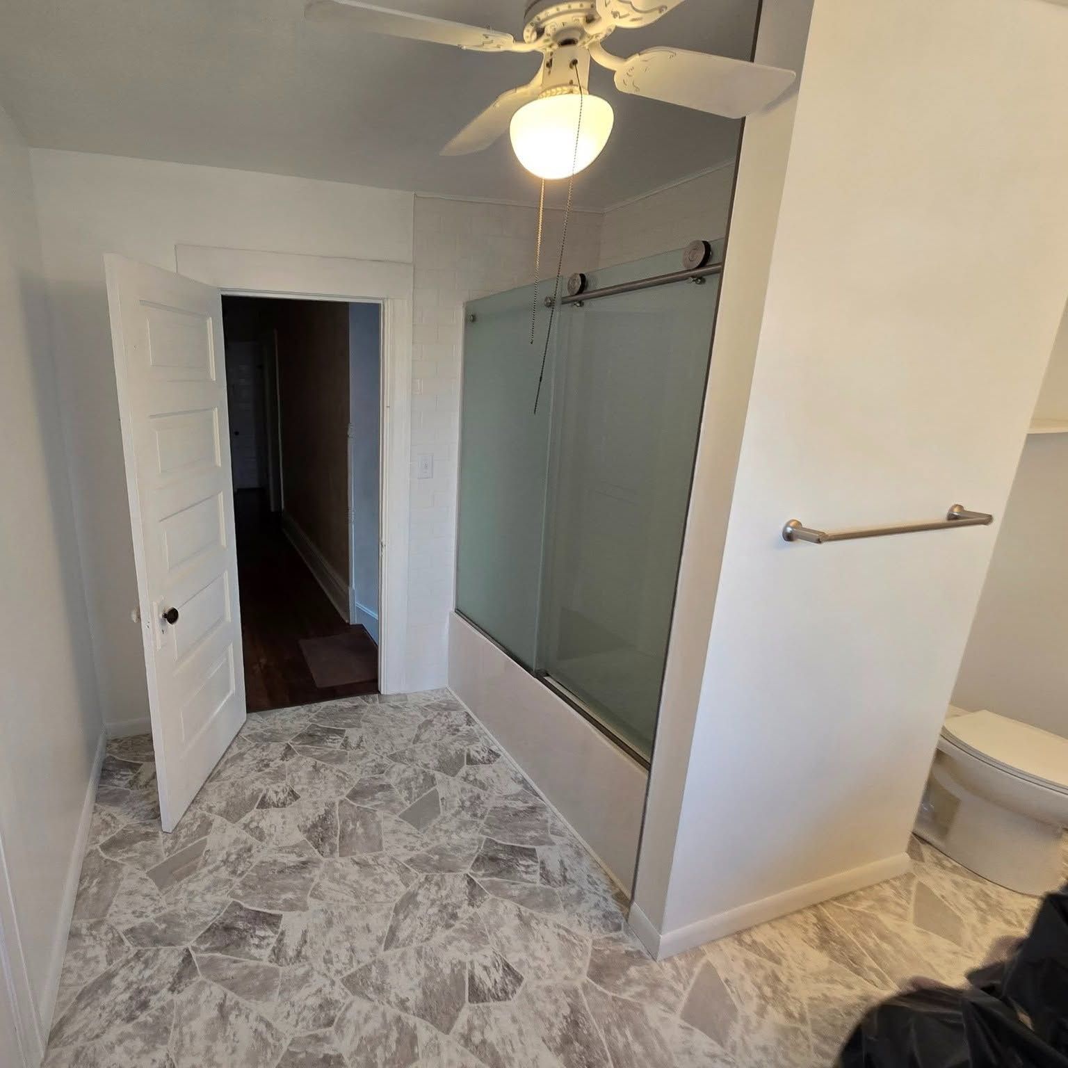 Bathroom with marble floor, frosted glass shower, ceiling fan, and an open doorway to a dark hall