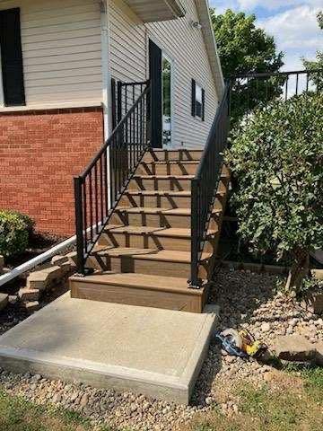 Exterior stairs with black railings leading to a side entrance beside a brick-and-siding house