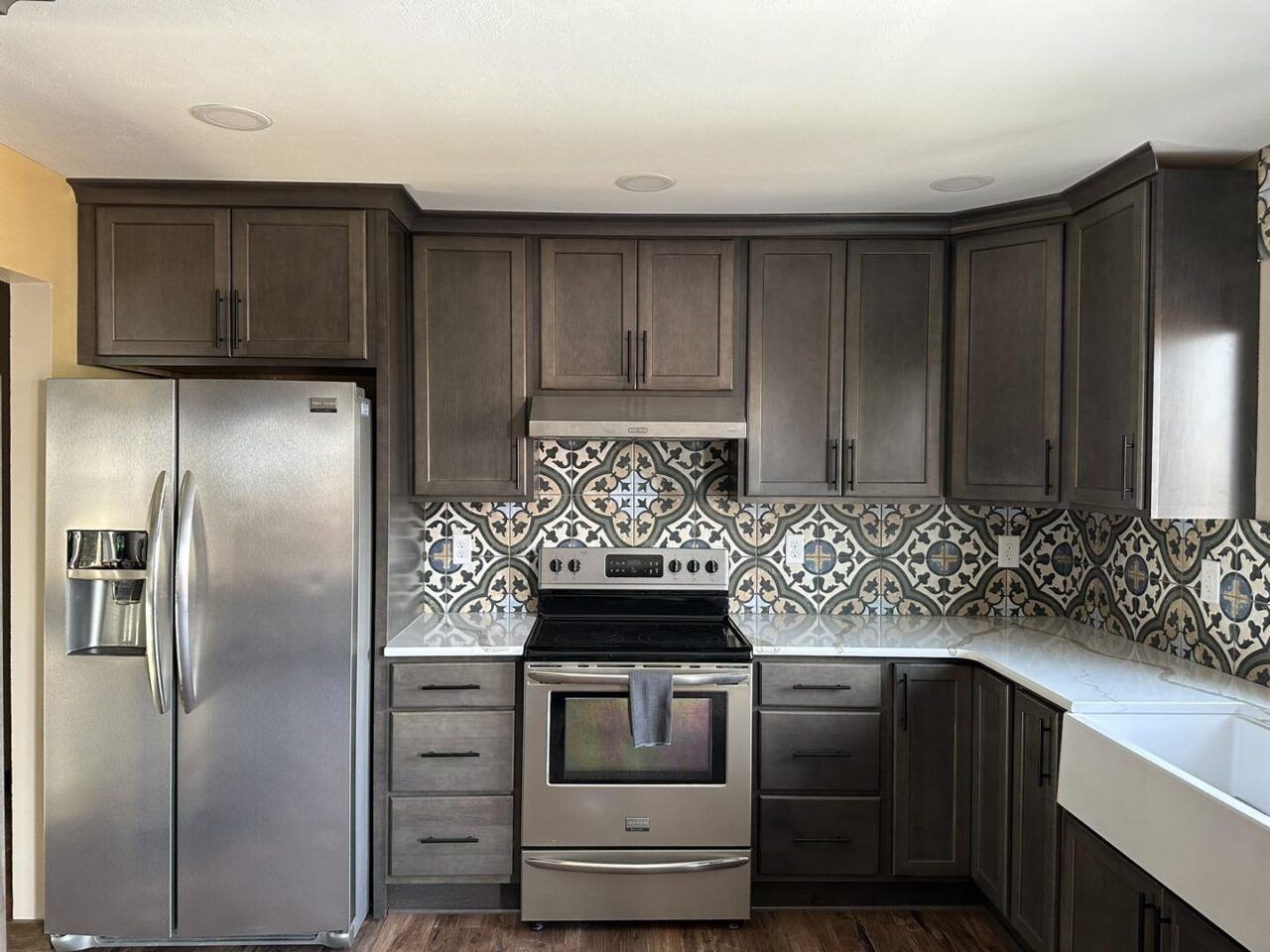 Modern kitchen with dark cabinets, stainless steel appliances, patterned backsplash, and white countertops
