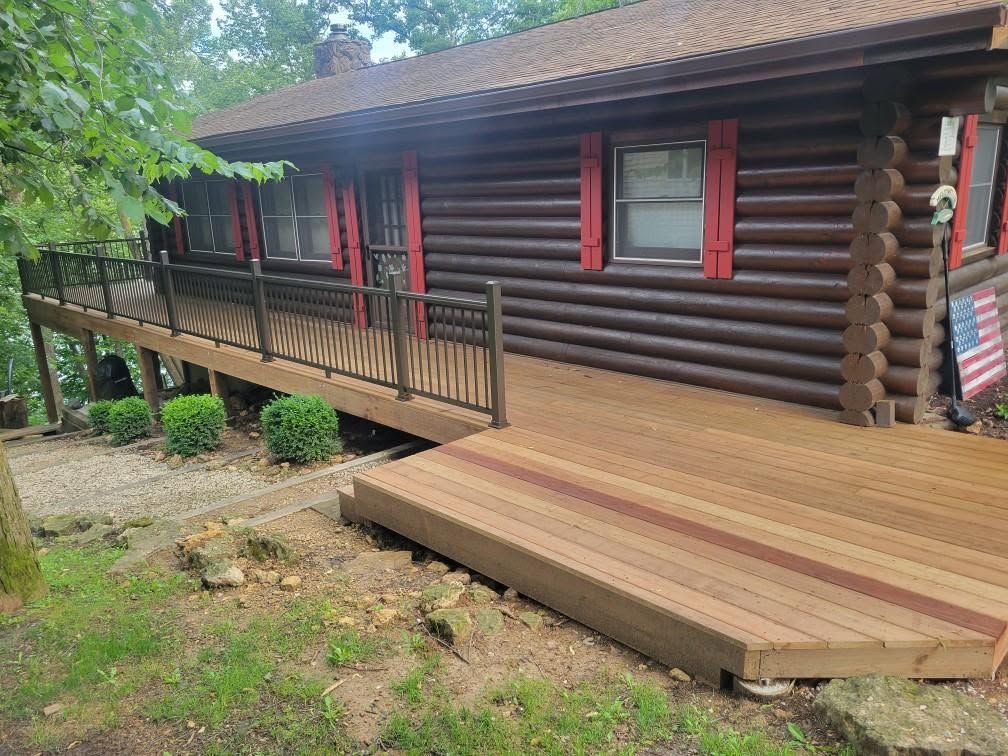 Log cabin porch with wooden ramp and red-shuttered windows surrounded by greenery