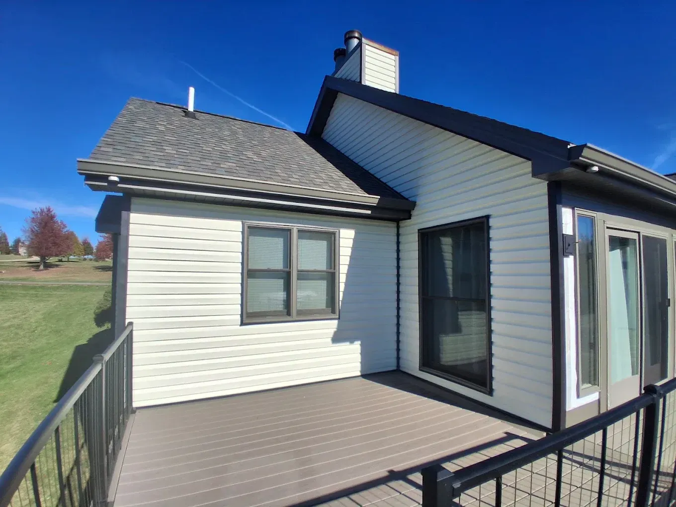 House exterior with white siding, dark roof, and a small deck under a clear blue sky
