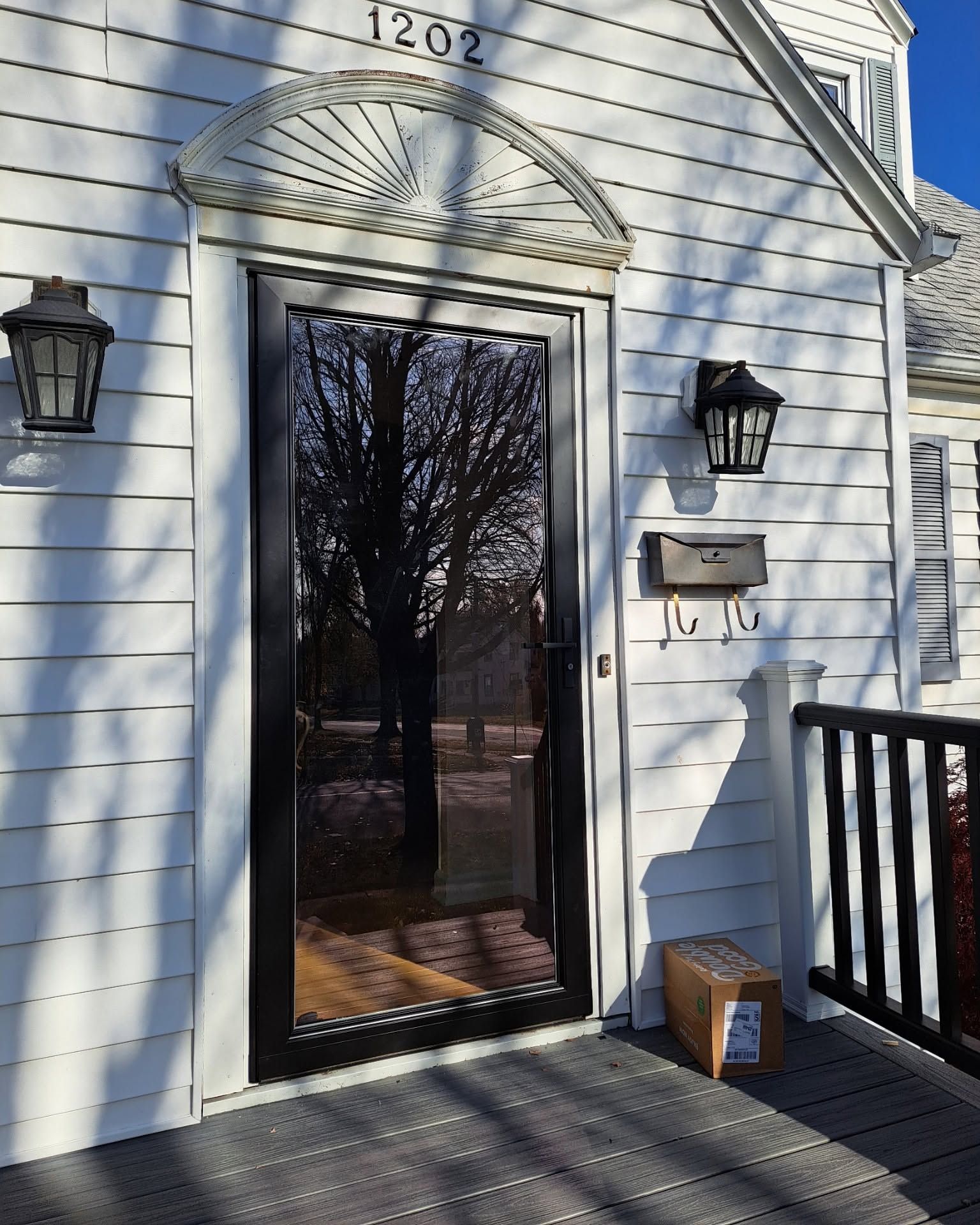 Front door of a white house with black trim, house number 1202, and a package on the porch