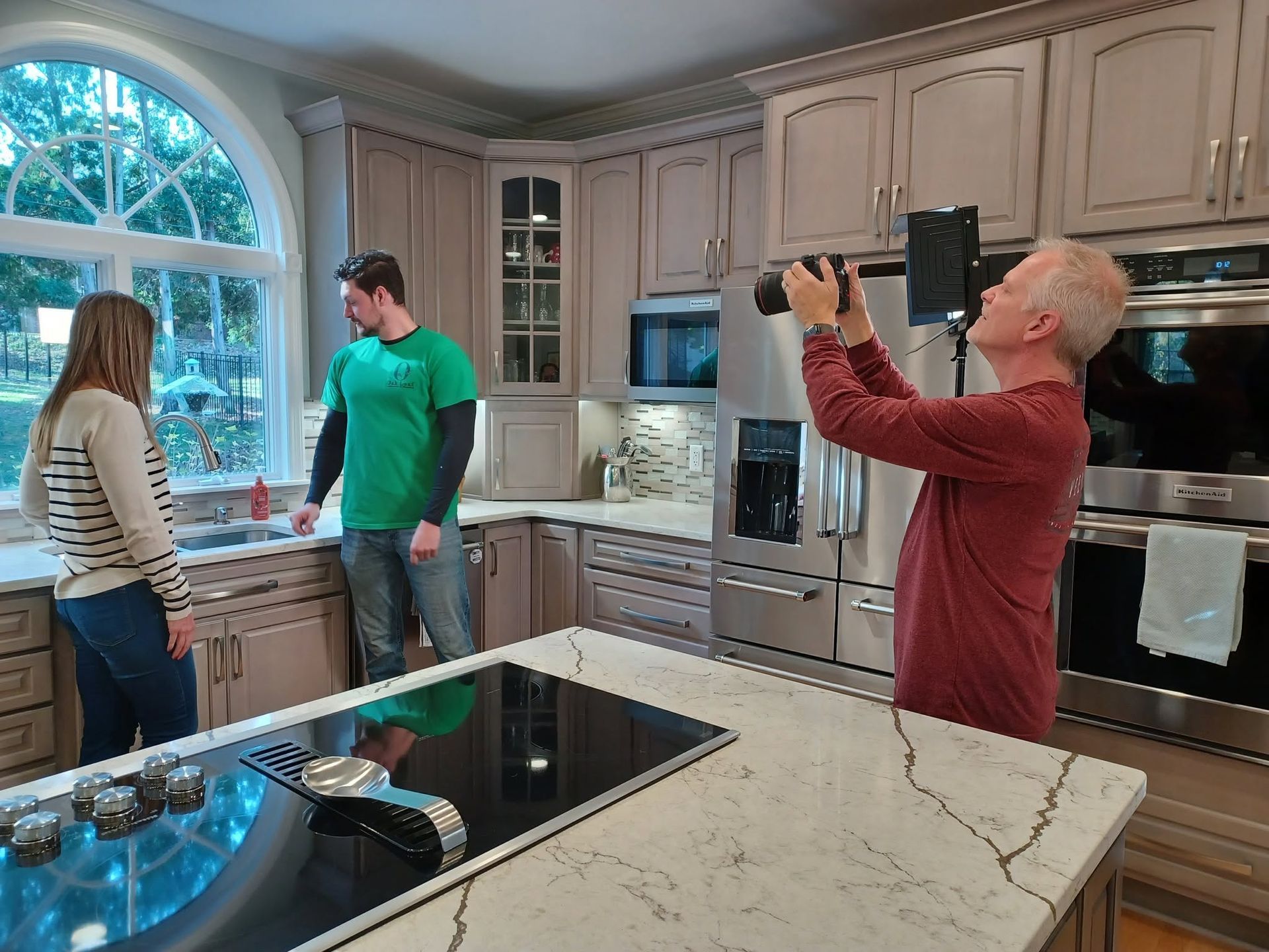 People in a bright kitchen posing for a photo near a large island and stainless-steel appliances