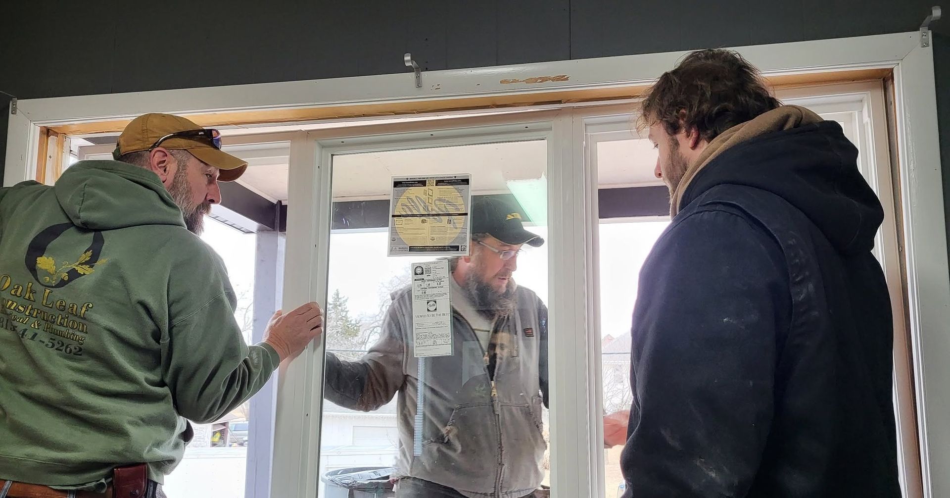 Three people talking at a doorway under construction, with one holding the door open.