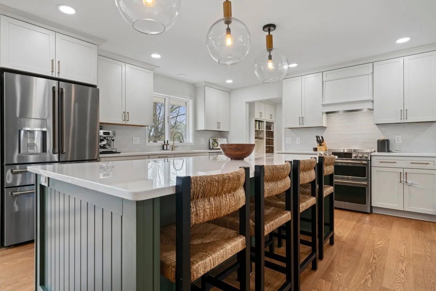Modern white kitchen with stainless steel appliances, island seating, and pendant lights