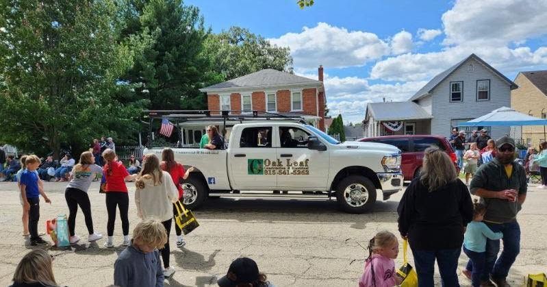 People watching a decorated white truck at a small-town parade on a sunny street.