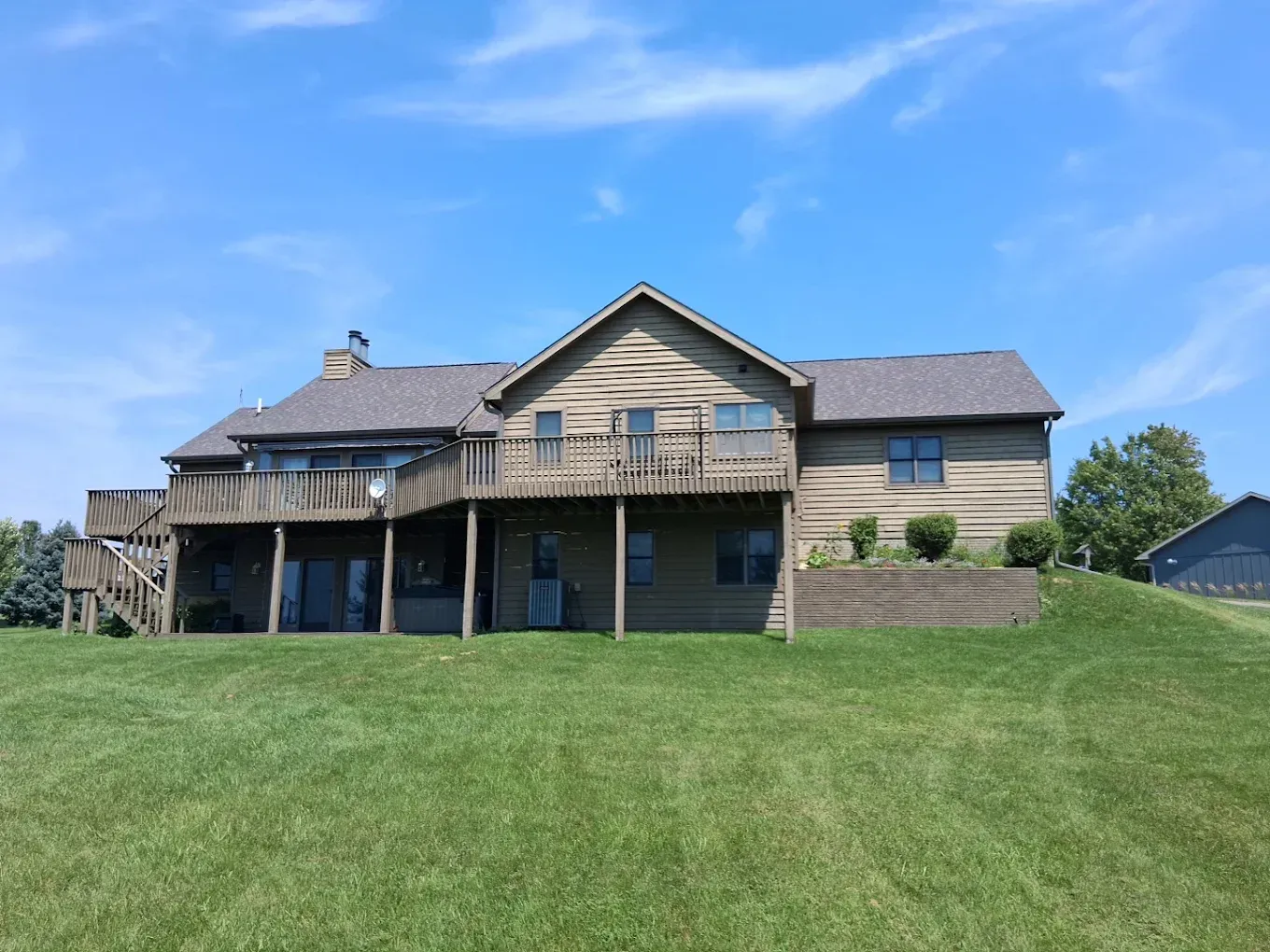 Large beige house with a deck on a grassy hill under a blue sky