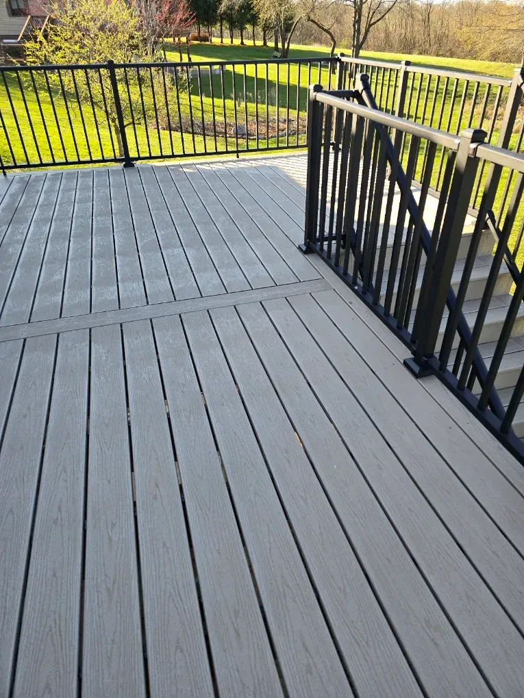 Gray deck with black railings overlooking a green park and walkway