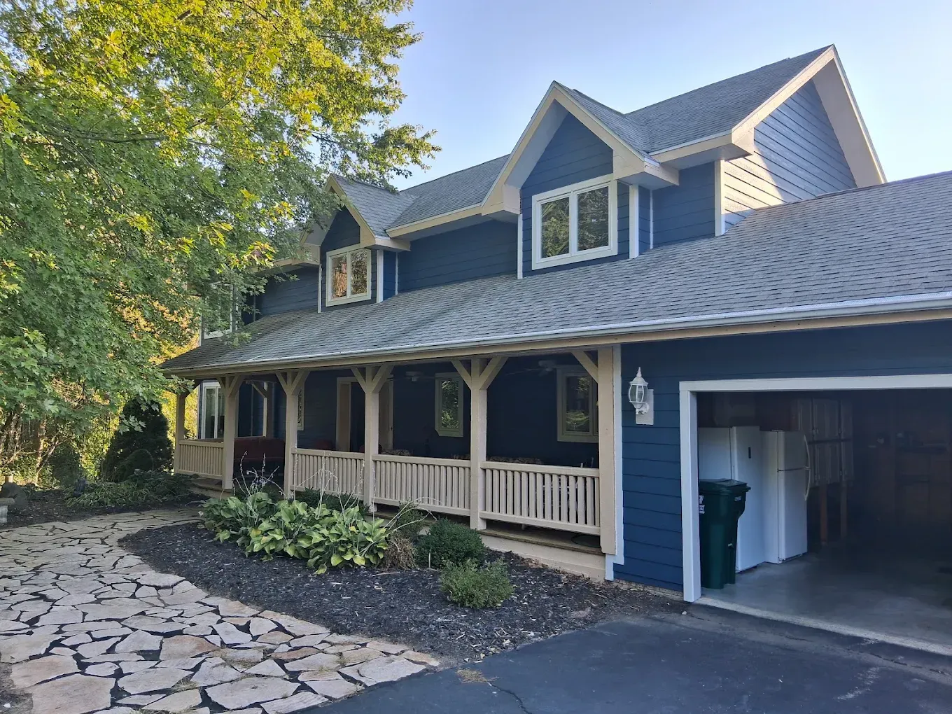 Dark blue house with white trim, front porch, and an attached garage beside a stone driveway.
