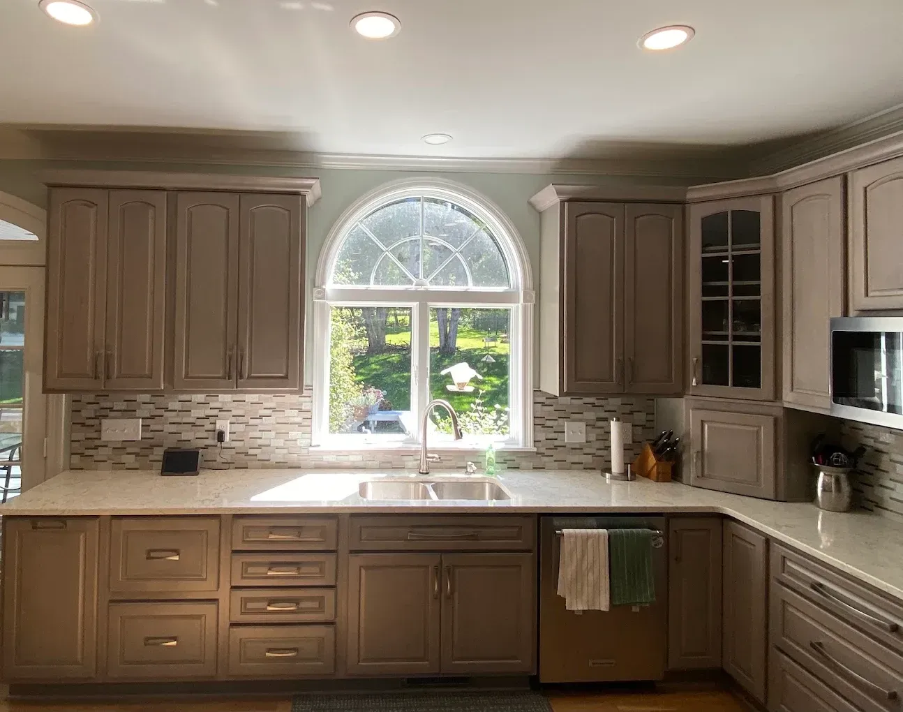Bright kitchen with light wood cabinets, granite counters, and an arched window above the sink.