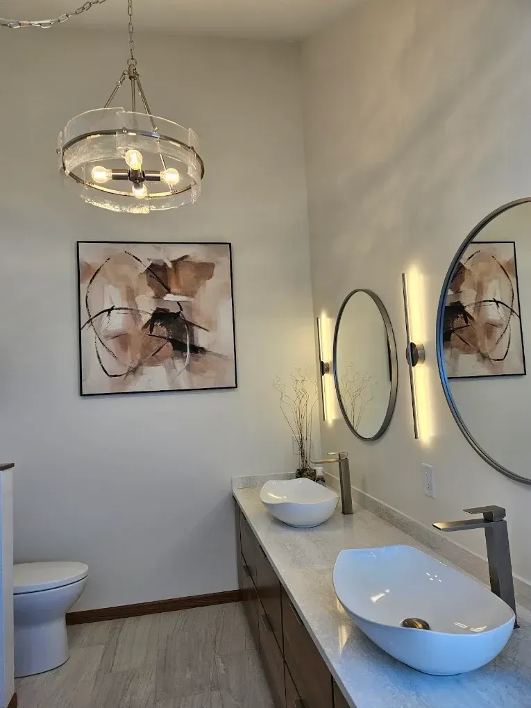Modern bathroom with two vessel sinks, round mirrors, wall art, and a pendant light