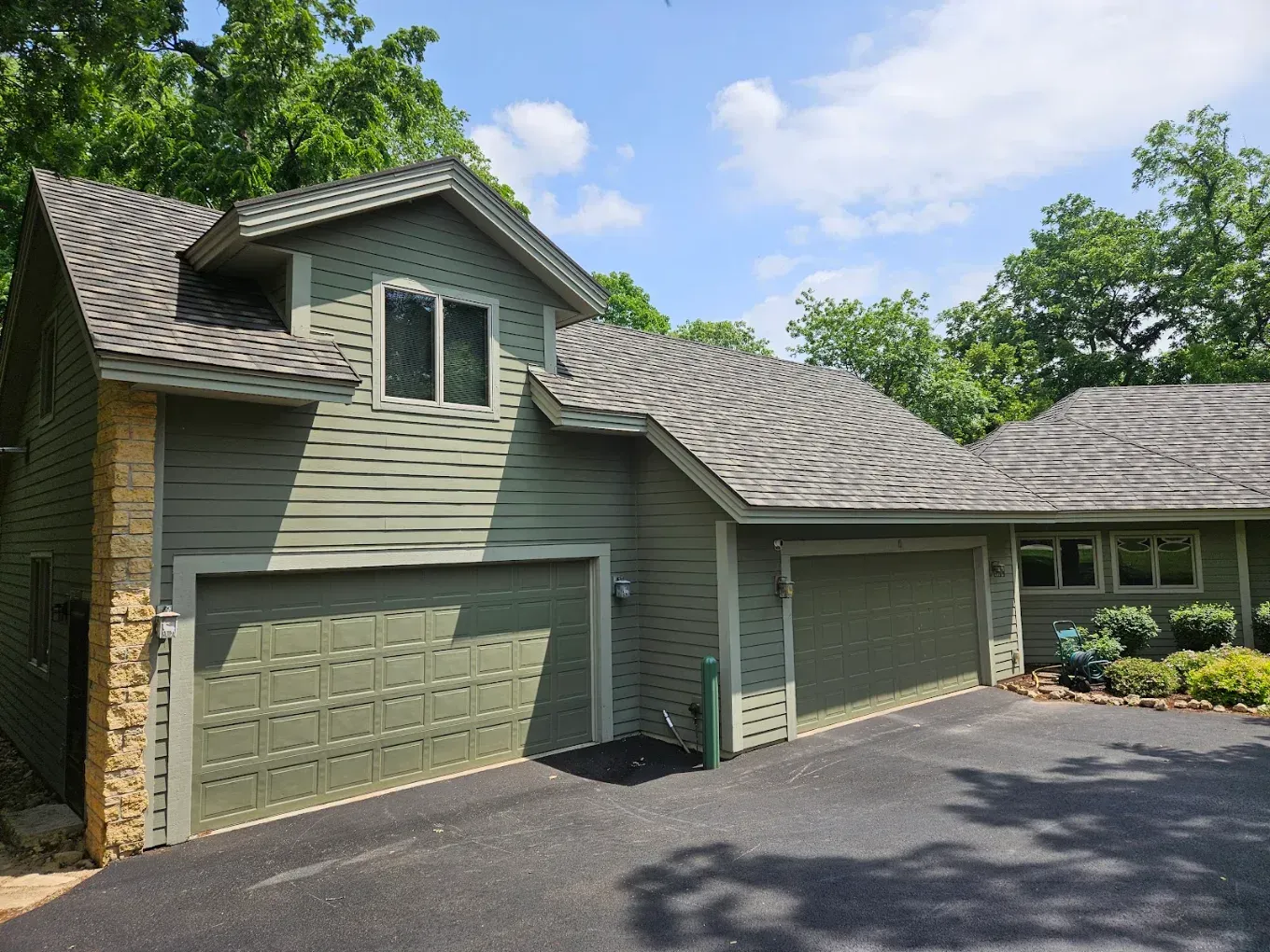 Green house exterior with three-car garage and driveway under sunny sky