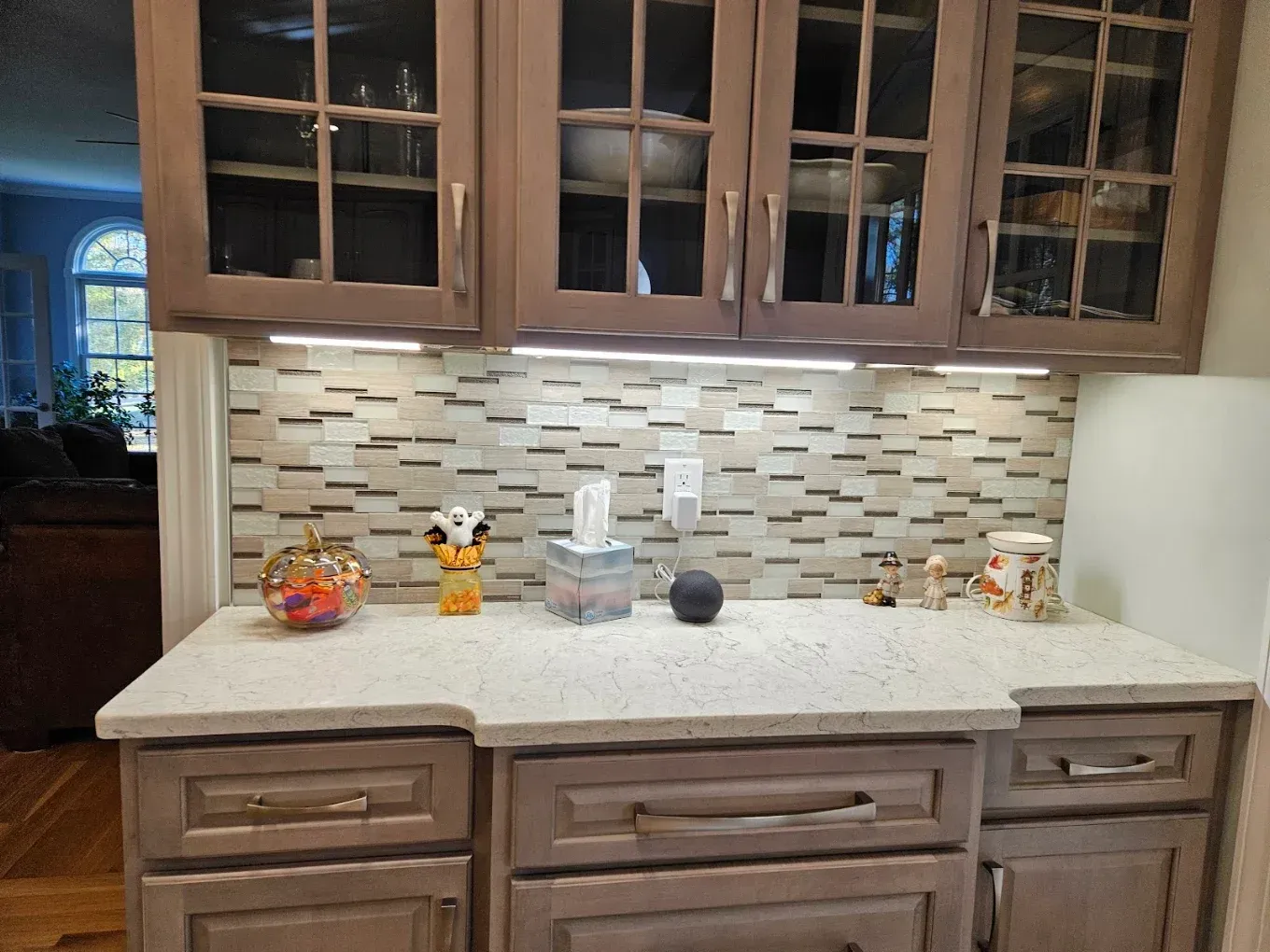 Wooden kitchen cabinets with glass doors above a speckled countertop and tile backsplash.