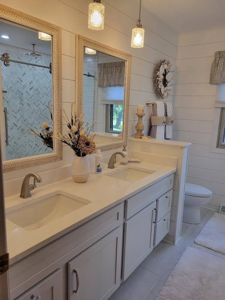 Bright white bathroom with double sink vanity, mirrors, pendant lights, and toilet.