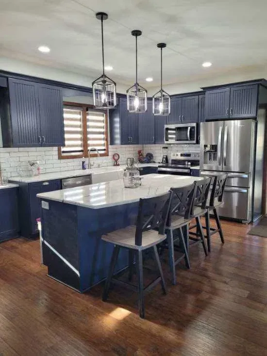 Modern kitchen with navy cabinets, white island, stainless appliances, pendant lights, and dark wood floors