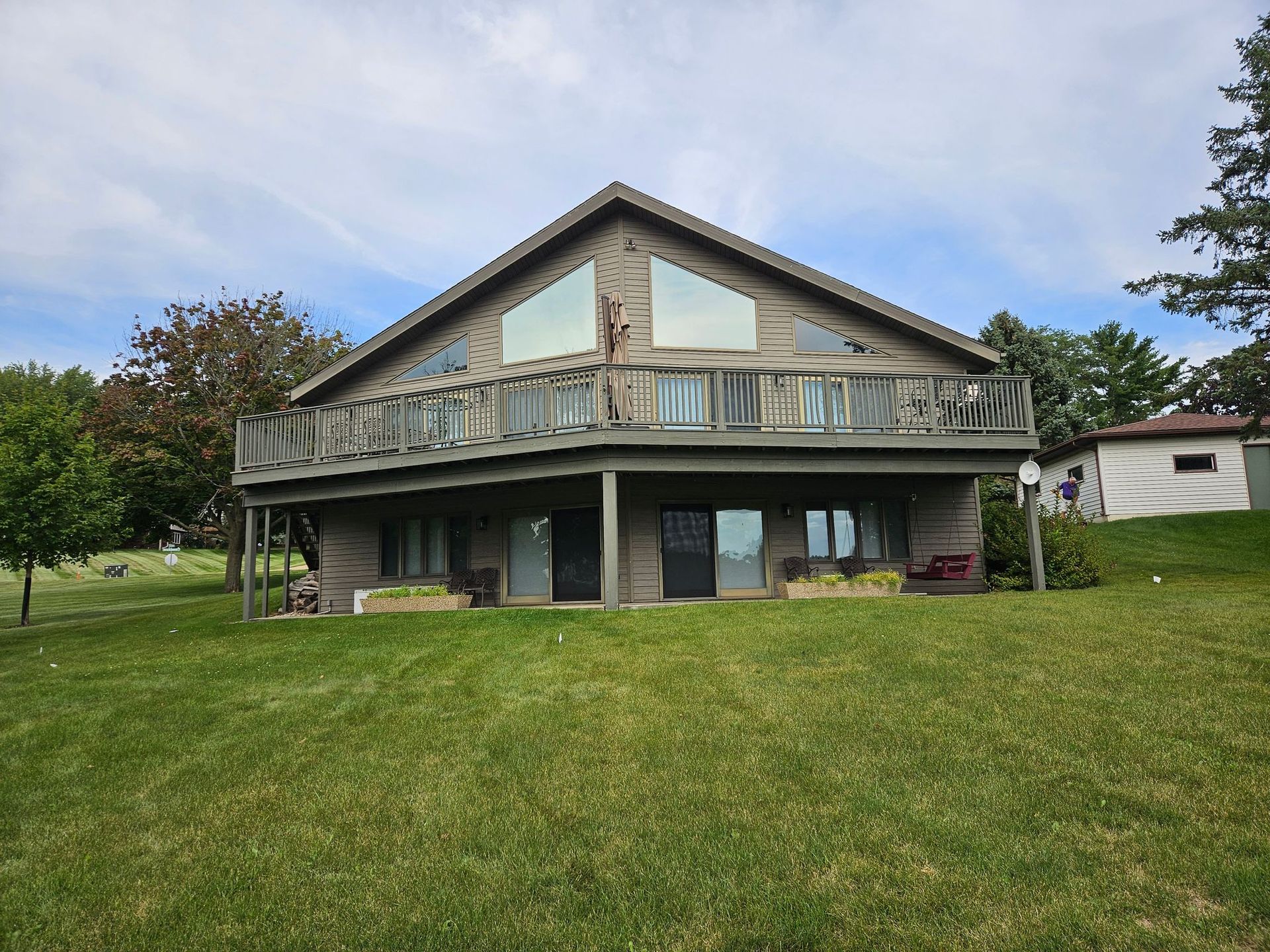 Two-story house with a covered deck, weathered wood siding, and a grassy yard under a cloudy sky