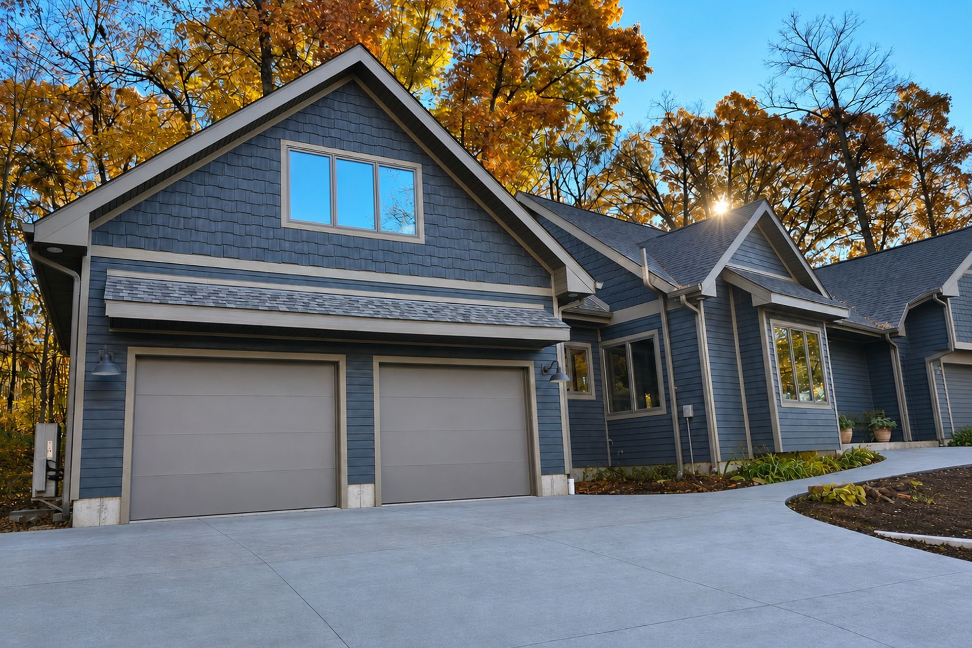 Gray modern house with two garage doors, stone accents, and autumn trees in the background