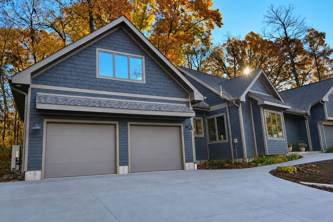 Gray modern house with two garage doors, stone accents, and autumn trees in the background
