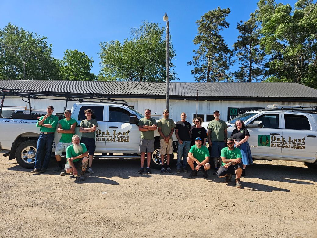 Group in green shirts posing beside white pickup trucks in a sunny gravel lot